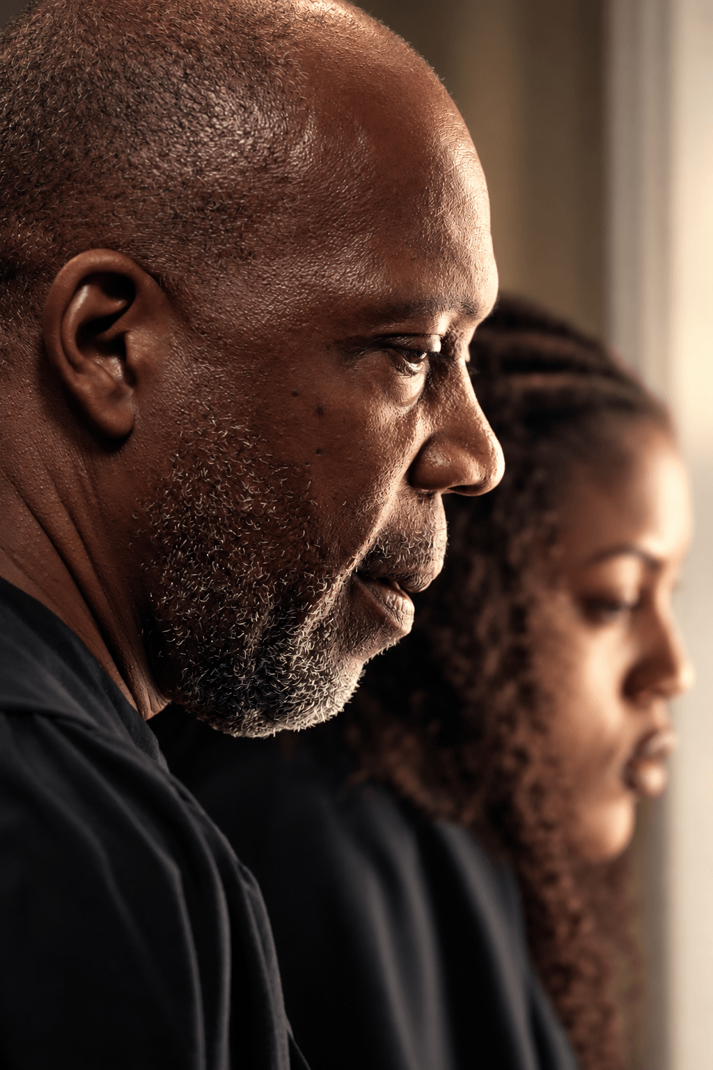 Close-up of an older man and a young girl looking out a window, side profile, natural light, serious expressions.
