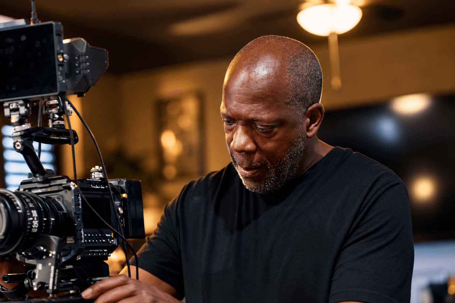 Man operating a professional camera indoors, focused on filming or photography, with warm lighting in the background.