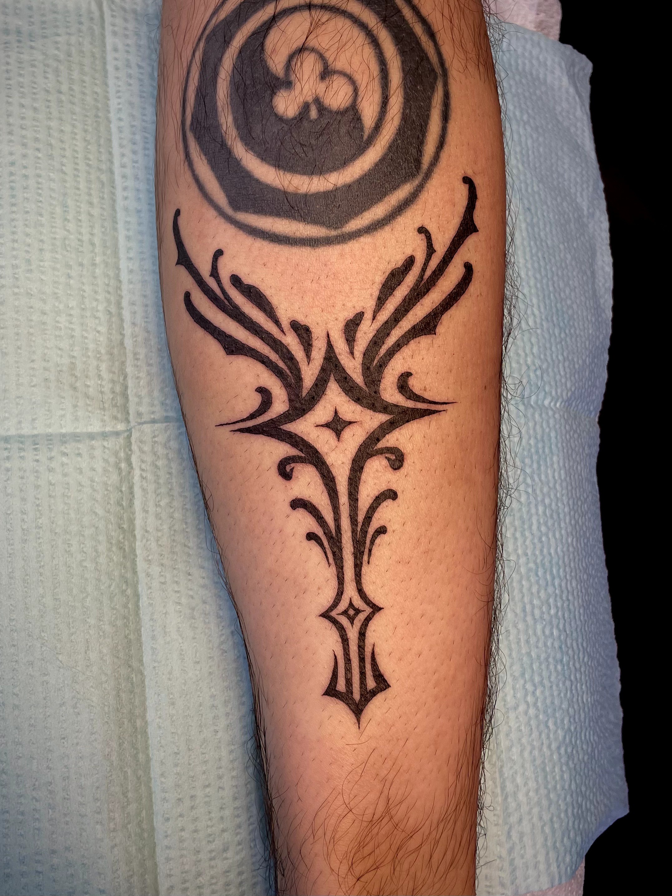 Tattoo with circular design at top and symmetrical tribal patterns extending downward on arm.