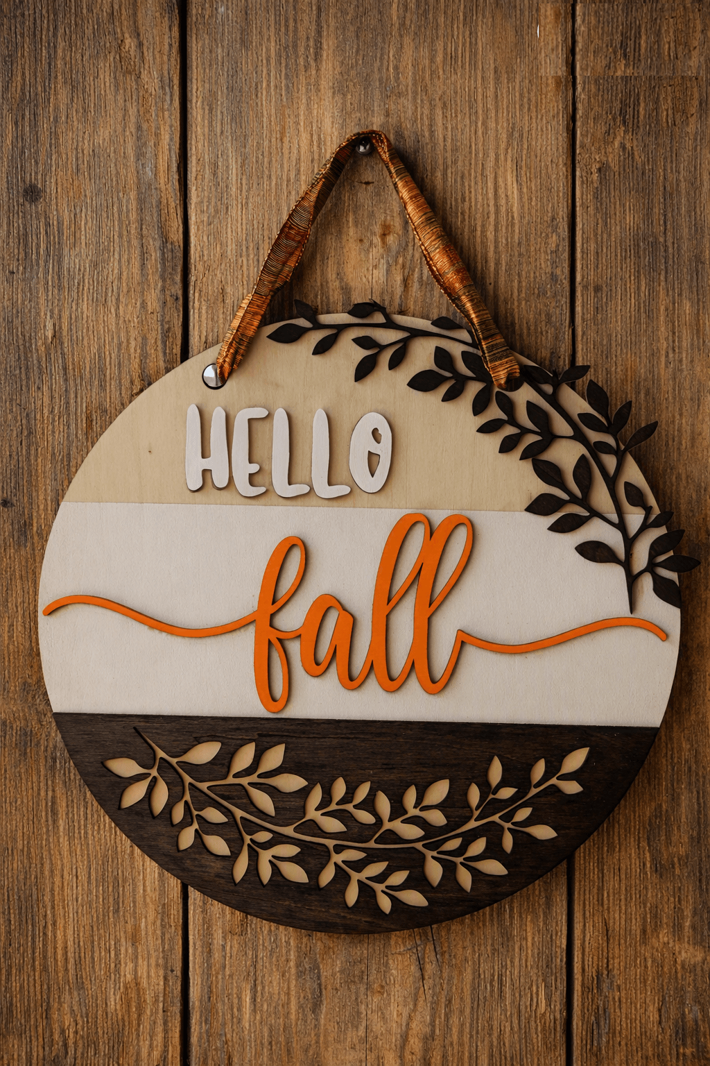 Round decorative sign with 'HELLO fall' text, leaf designs, hanging on wooden wall