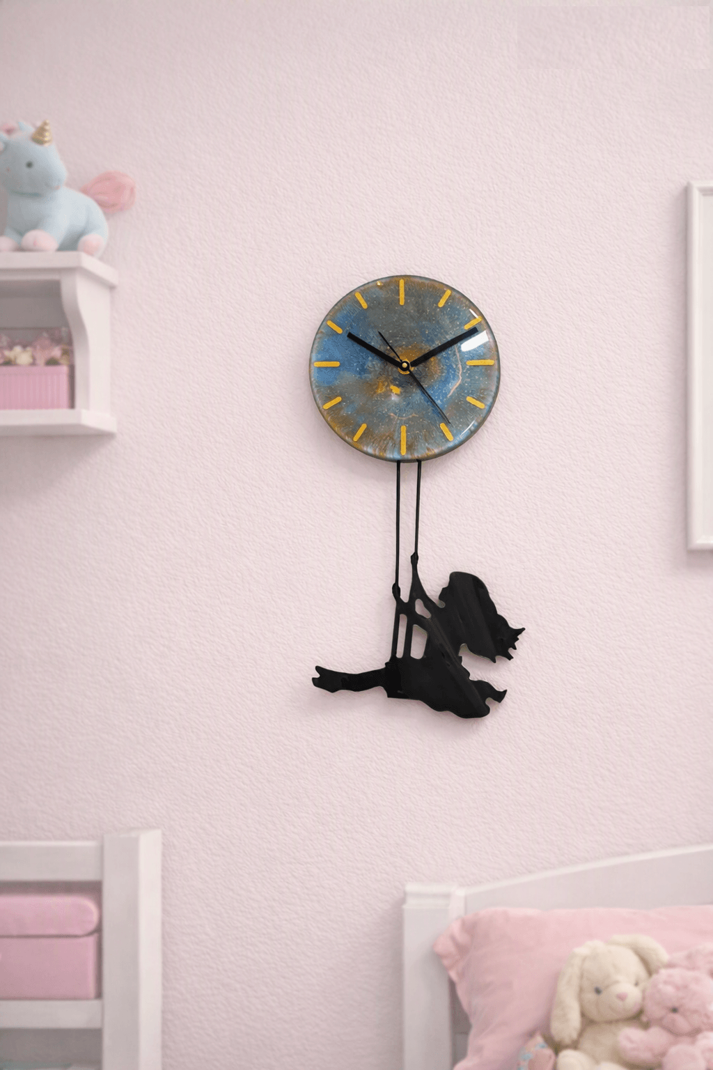 Wall clock with a blue face and yellow markings, hanging above a black plush dog toy, in a pink-themed room.