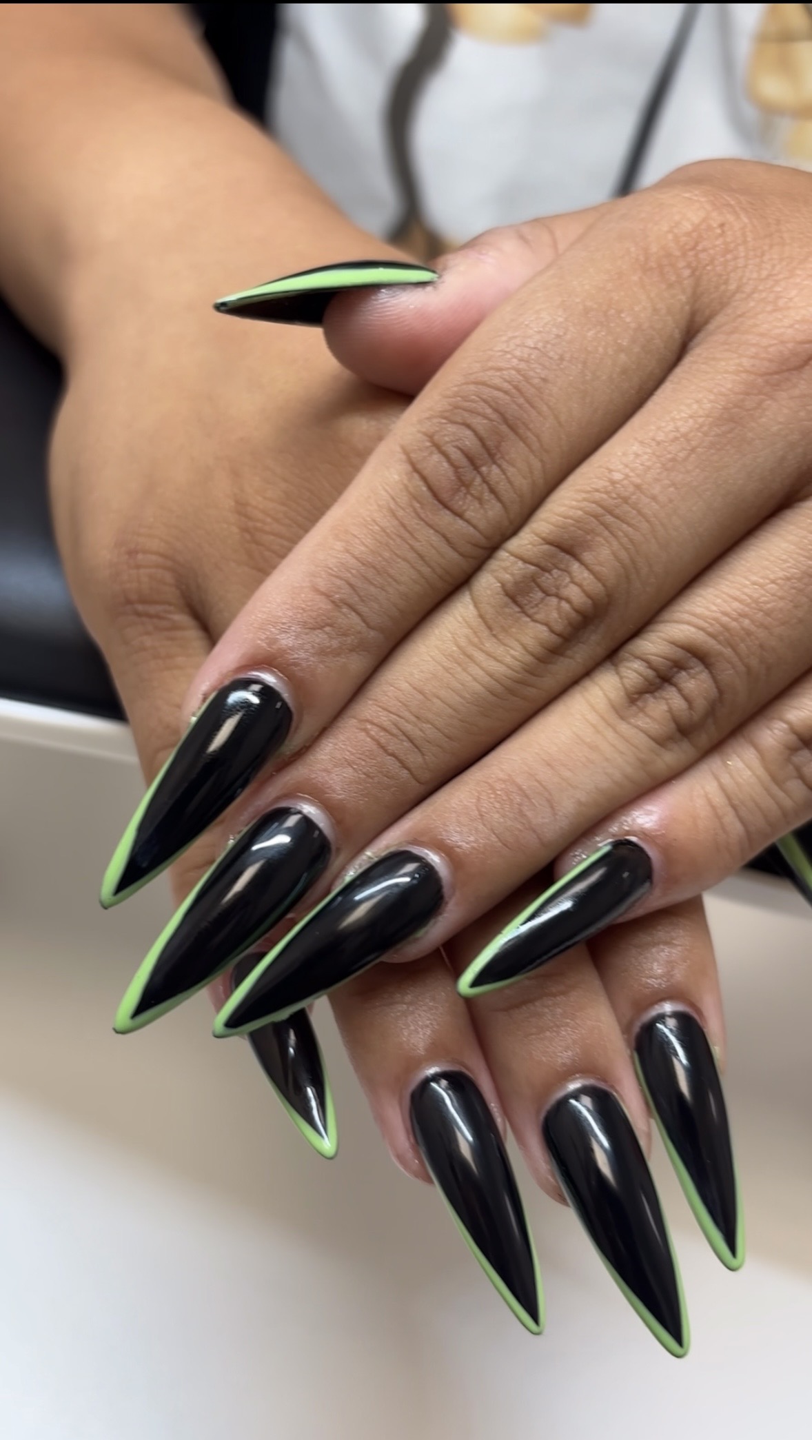 Close-up of hands with long, black nails with green tips, resting on a surface.
