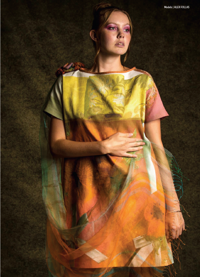 Young woman with makeup and a colorful dress, standing against a dark background, looking to the side.