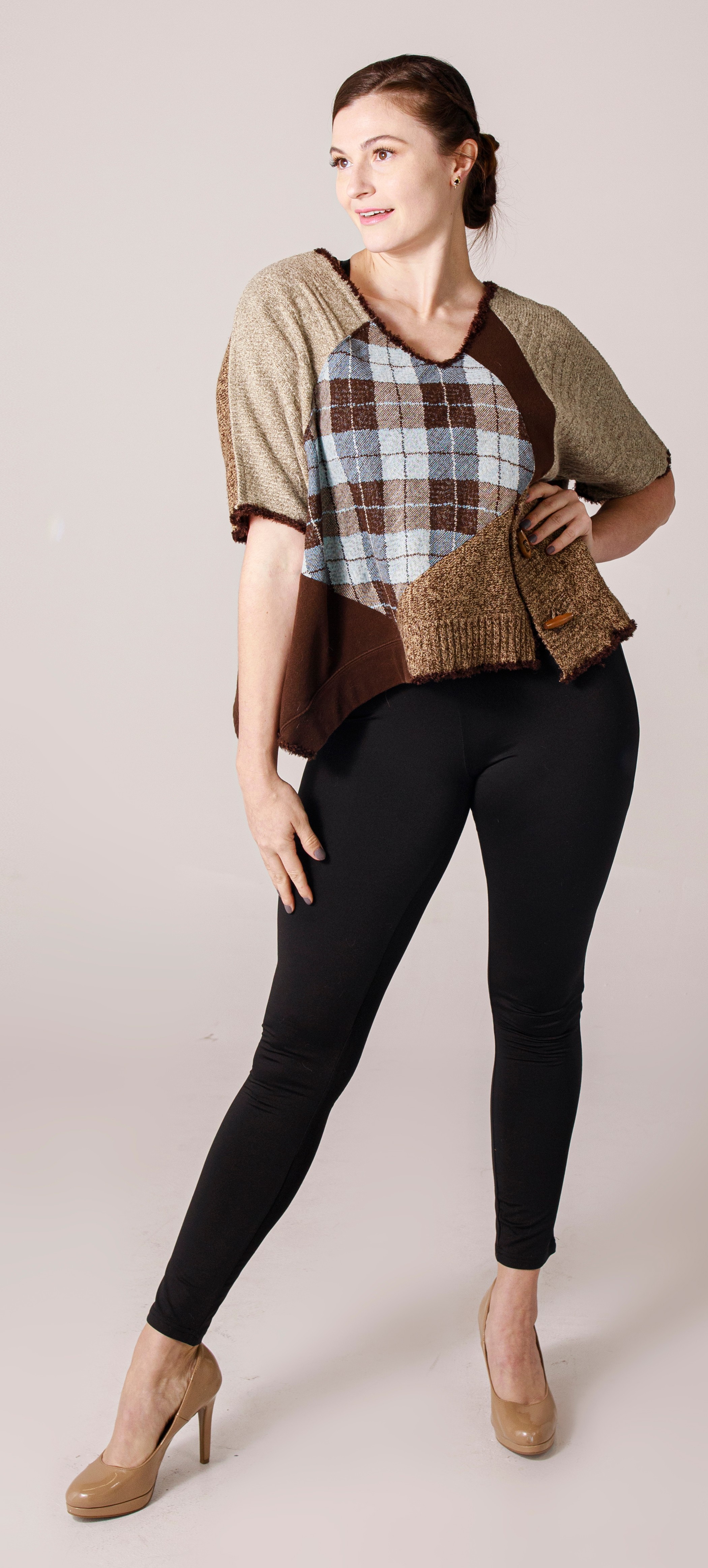 Woman in a patchwork sweater and black pants standing with hand on hip, neutral background.