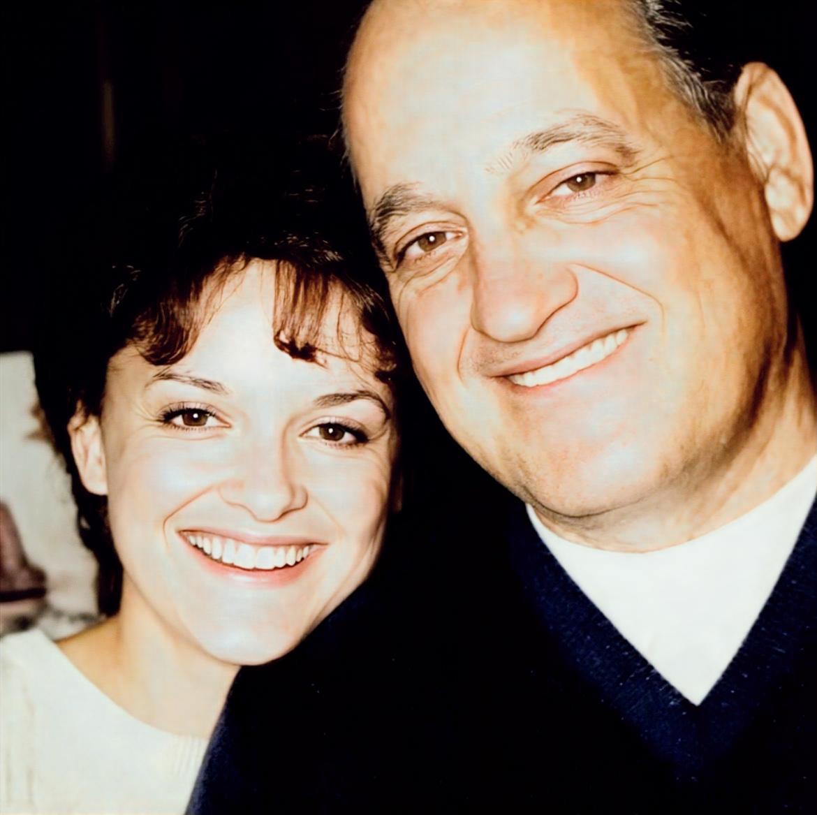 Two people smiling closely, with the woman on the left and the man on the right, both facing the camera.