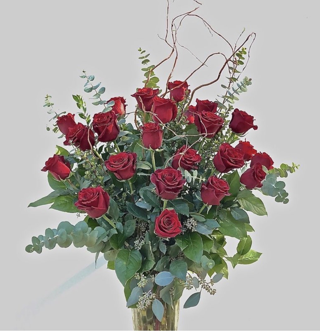 Bouquet of red roses with green leaves and curly twigs against a light background.
