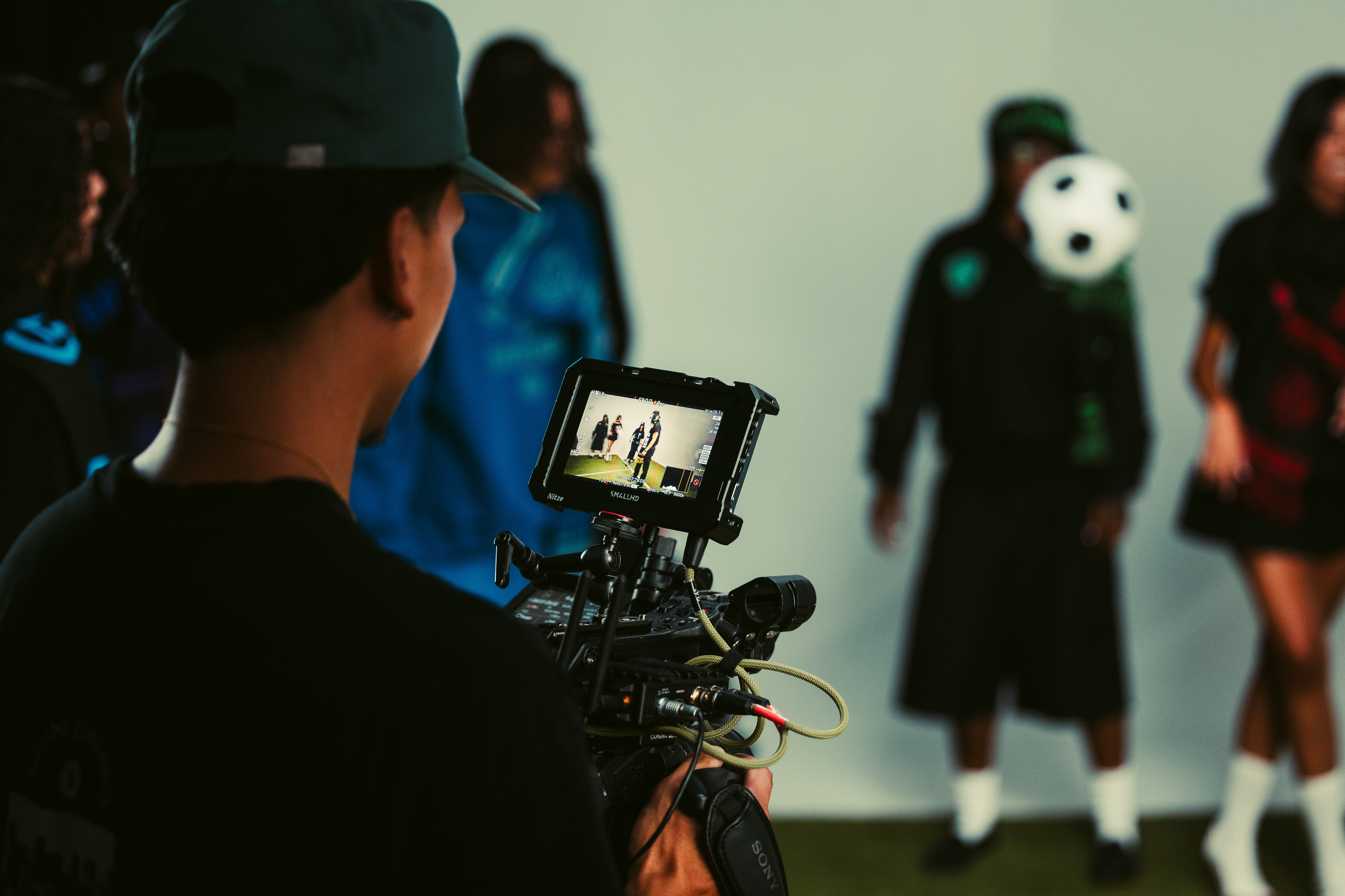 Person filming a group of people, one wearing a panda mask, against a plain background.
