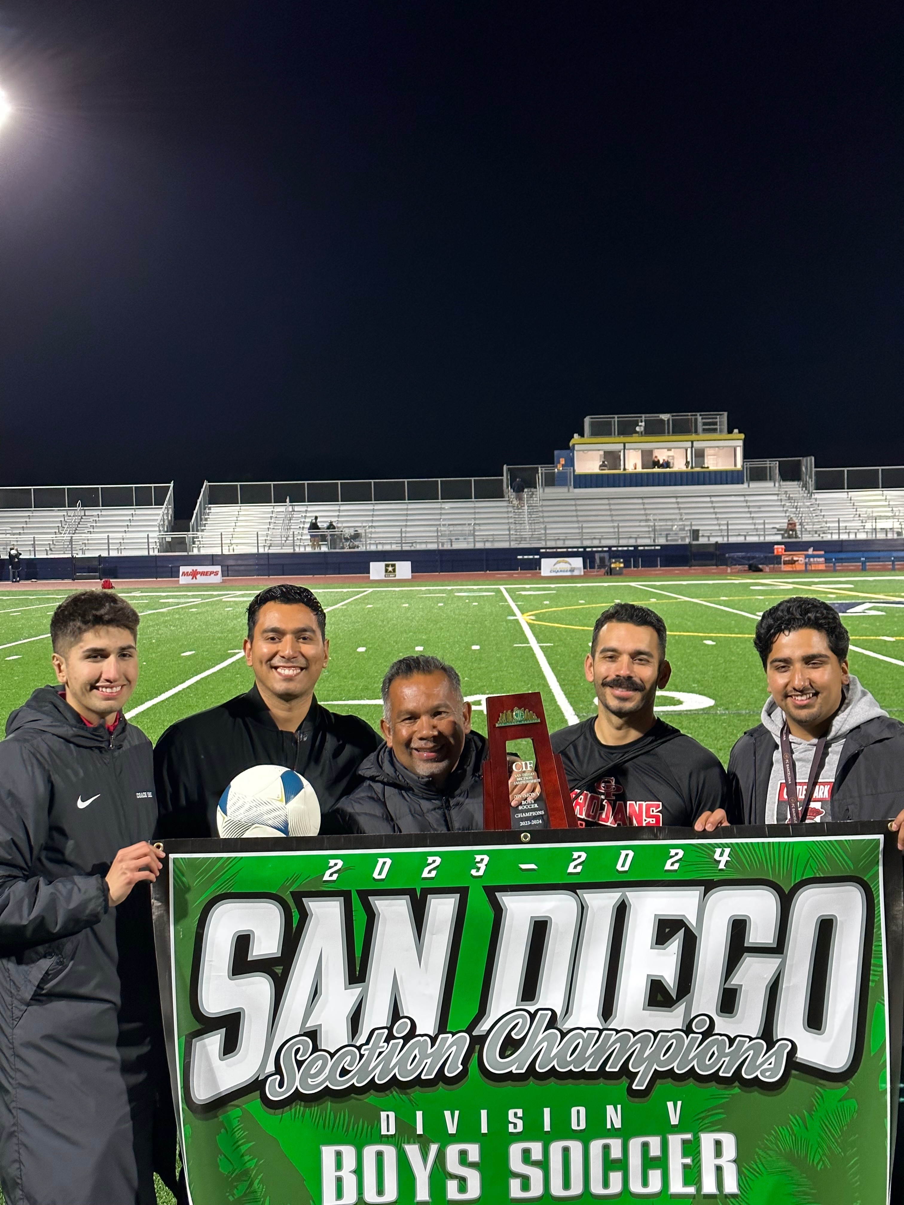 Five people standing on a soccer field holding a large sign that reads 'San Diego Section Champions 2023-2024 Division V Soccer'.