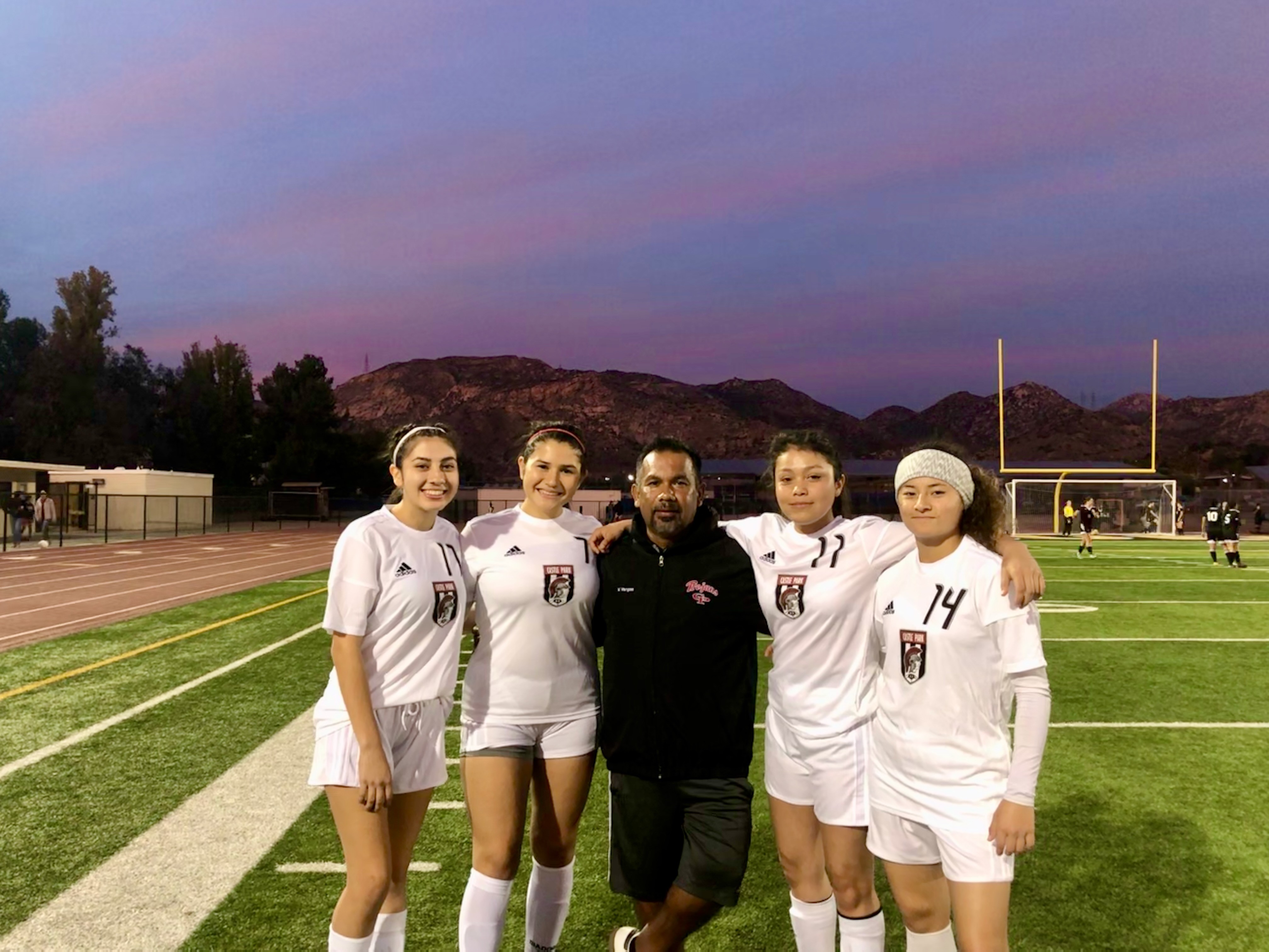 Group of five people standing on a football field during sunset, with mountains in the background.