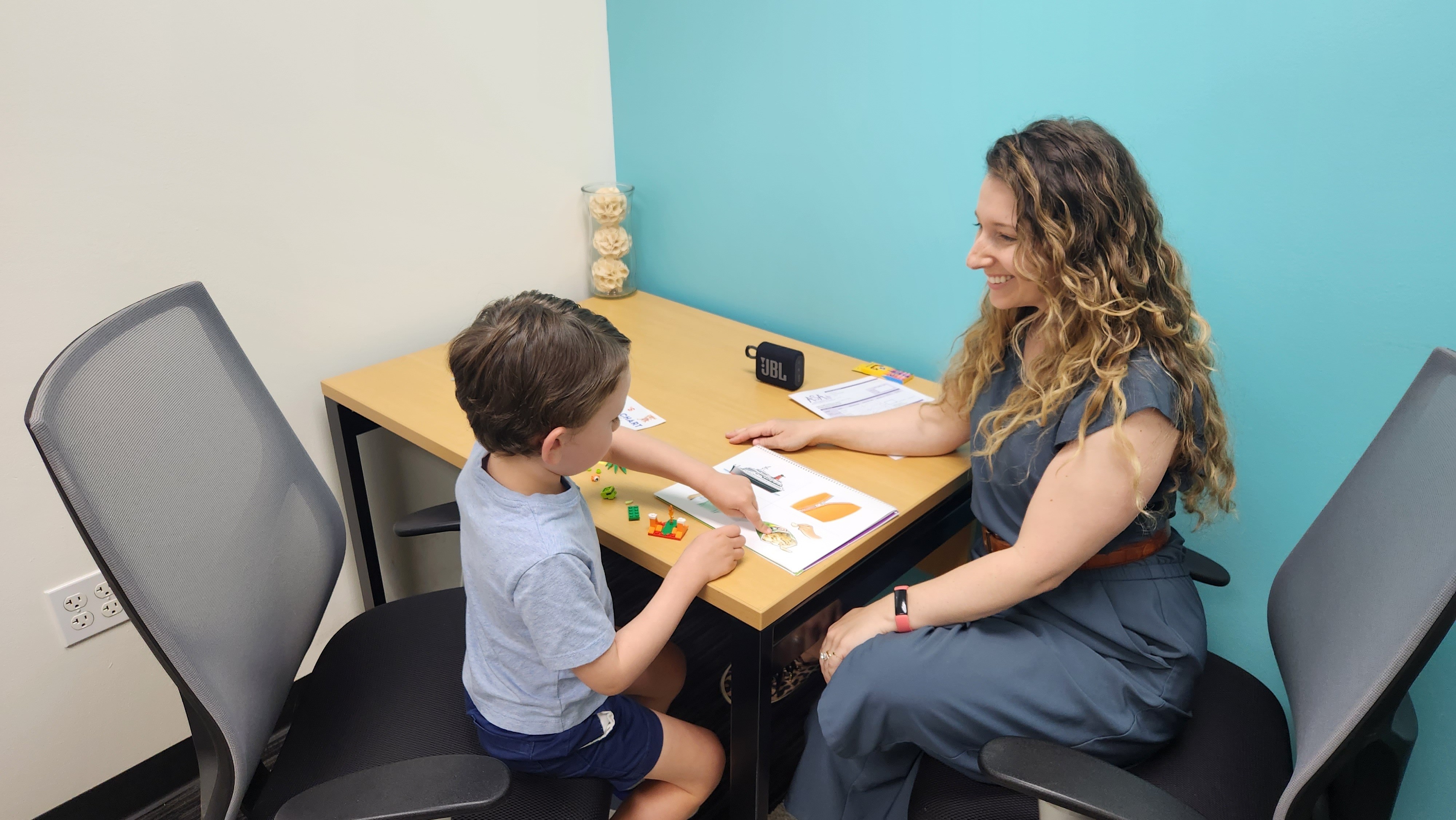 Child and woman sitting at a desk with papers, engaging in a discussion or activity.