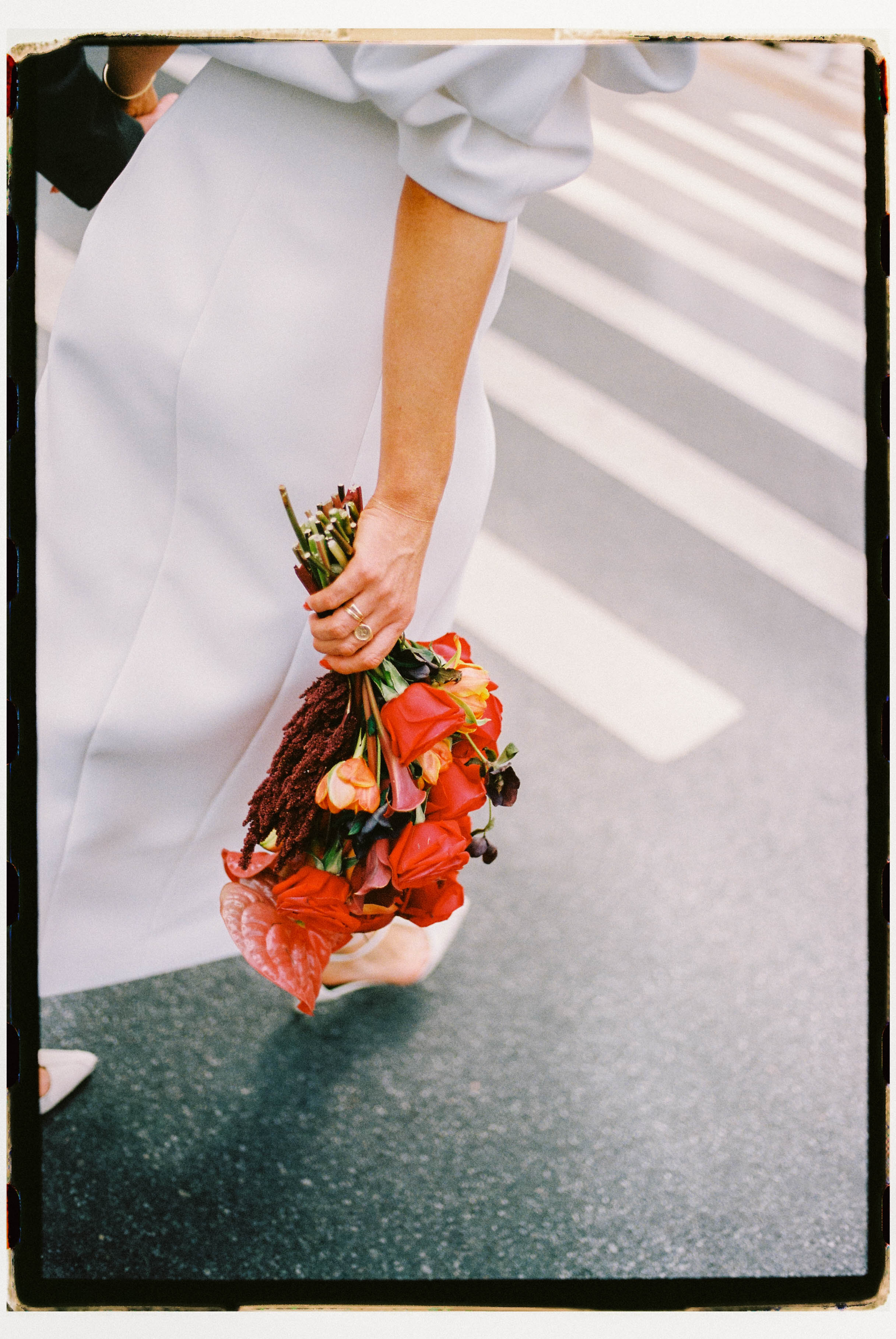 Person holding a bouquet of flowers on a city street crosswalk, wearing a white dress or coat sleeve.
