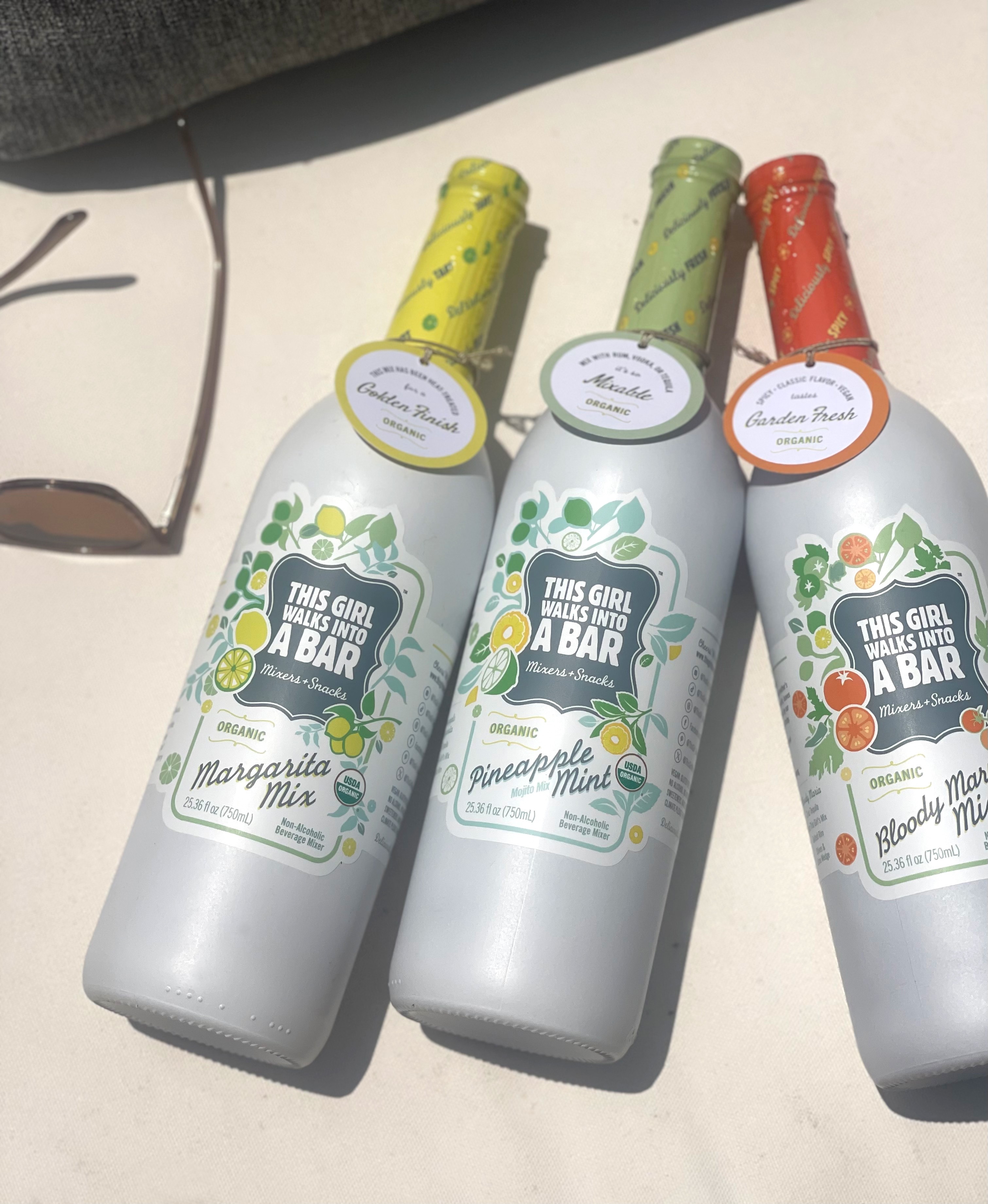 Three bottles with colorful caps and labels, placed on a white surface, partially shaded, with a book nearby.