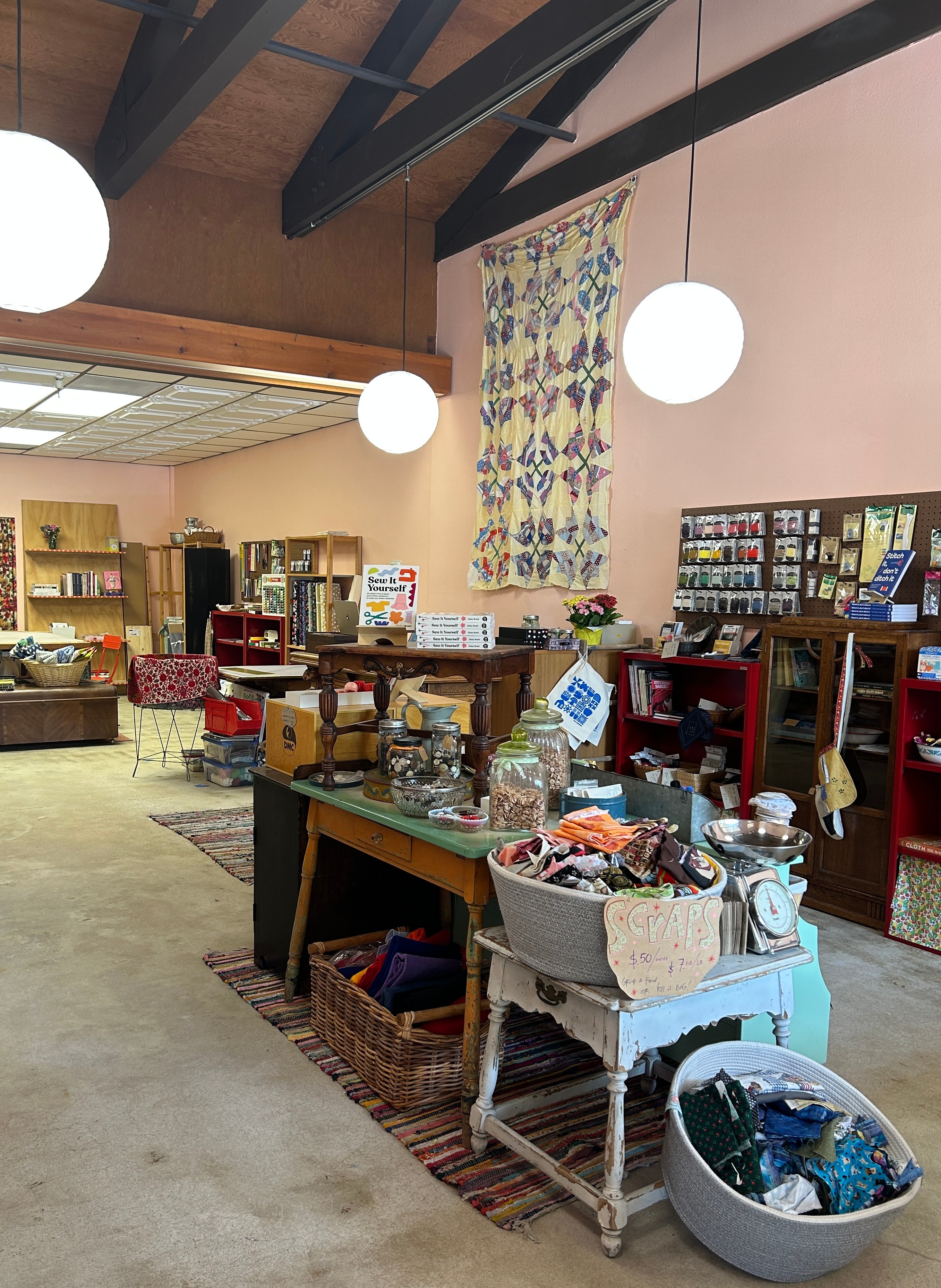 Interior of a thrift store with tables, shelves, and hanging lights, displaying various items for sale.