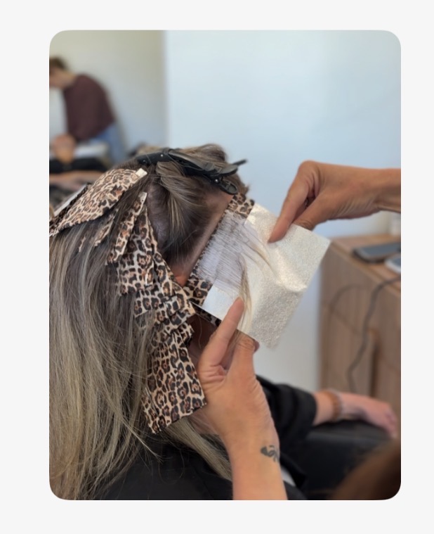 Person getting hair extensions applied, with hair clips and a towel on their head, in a salon setting.