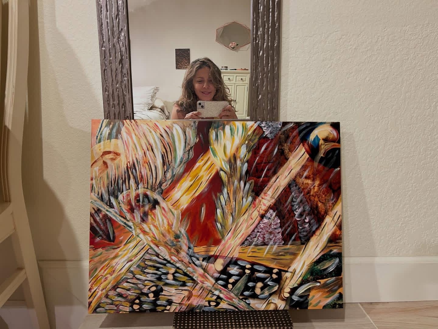 Person taking a photo of a colorful abstract painting in front of a mirror, with a woman visible in the mirror's reflection.