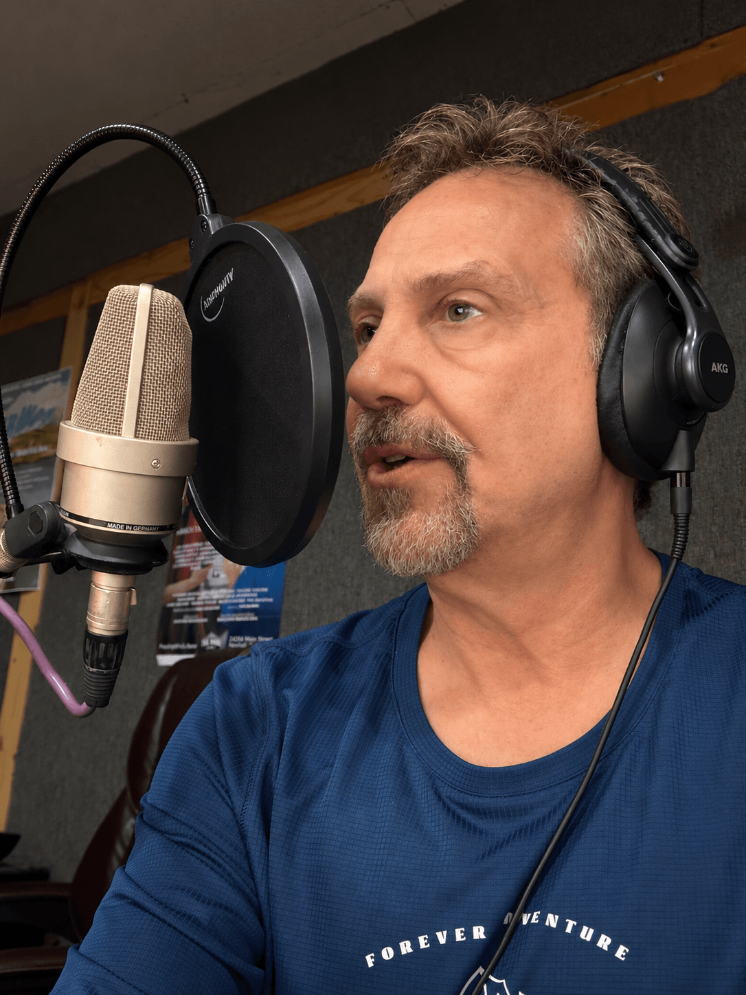 Man with headphones speaking into a microphone in a recording studio.
