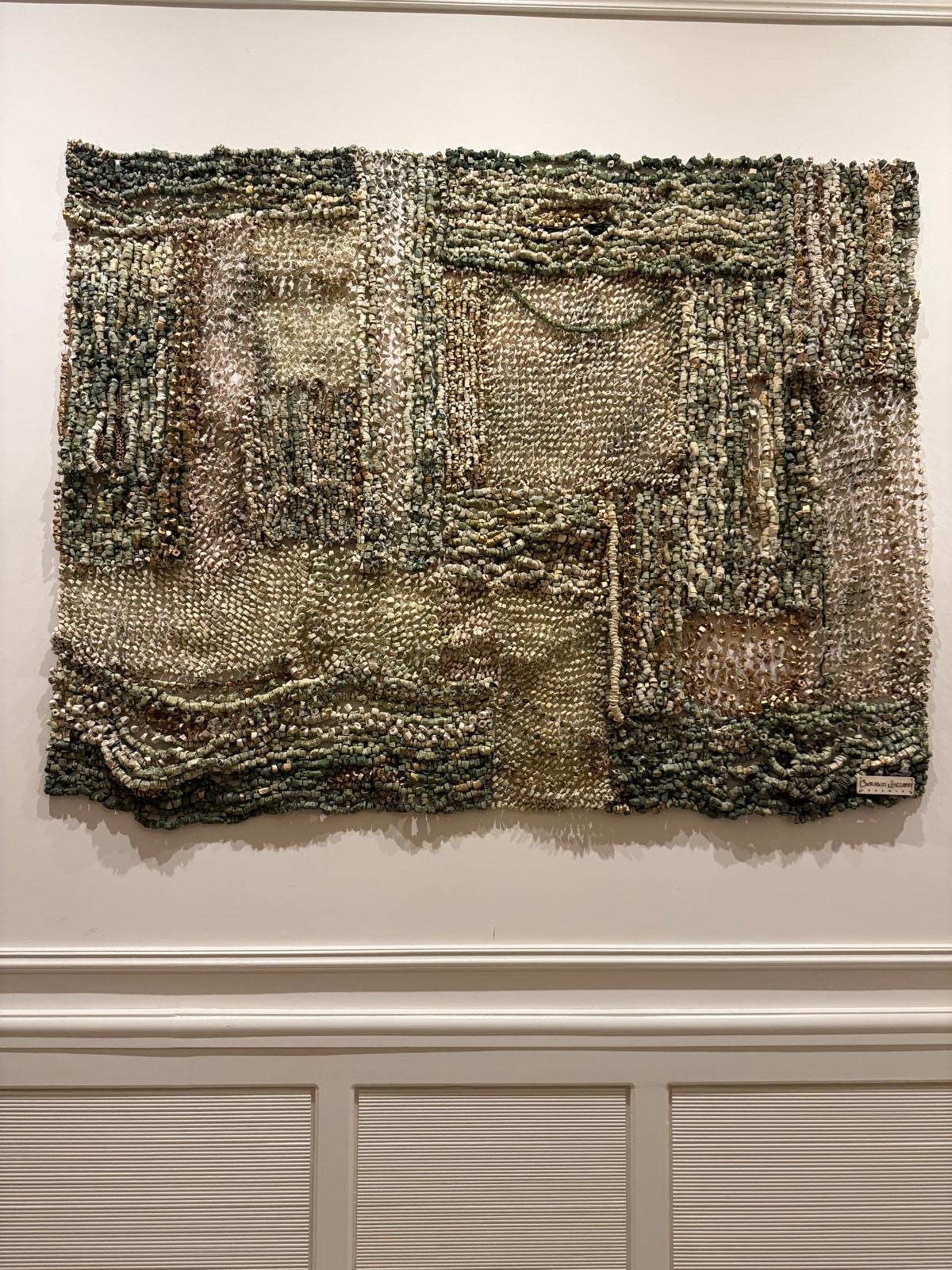 Textured abstract artwork with layered, earthy tones and intricate patterns on a white wall.