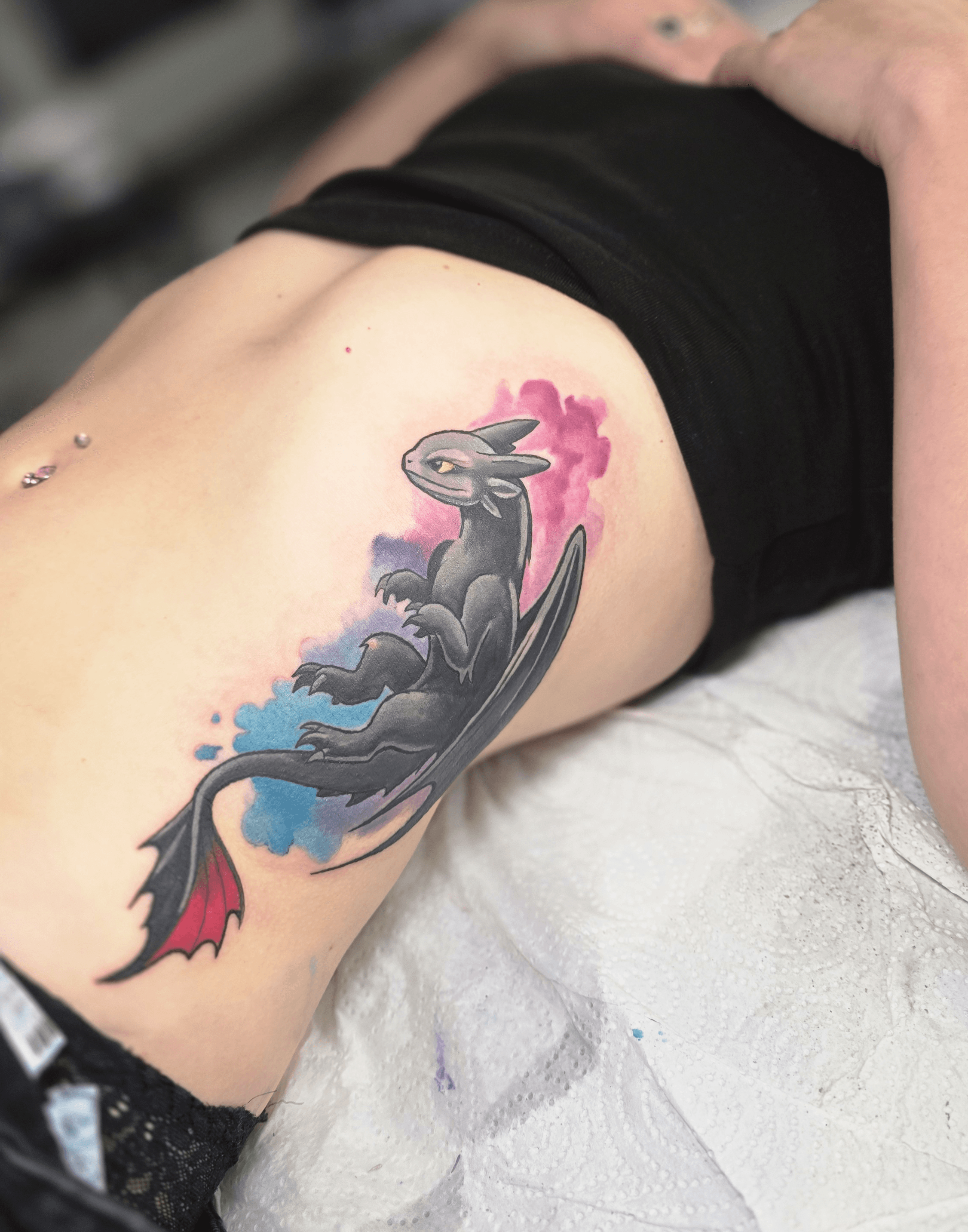 Tattoo of a black rabbit with a red-tipped tail, surrounded by pink and blue watercolor splashes on person's side.