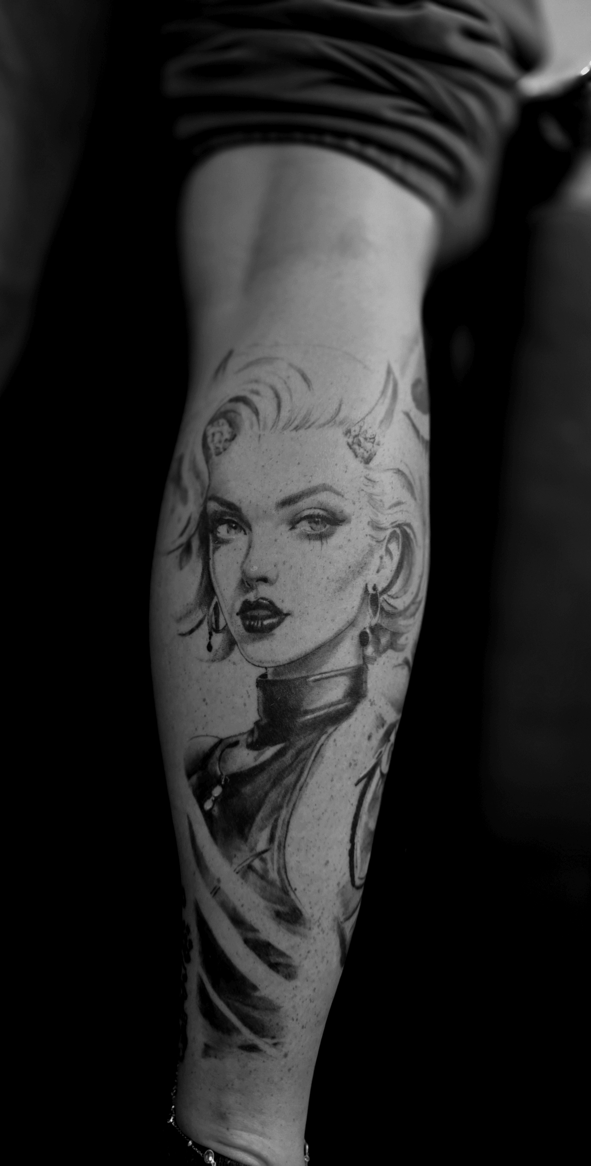 Black and white tattoo of a woman's face with wavy hair on forearm, detailed shading and expression.