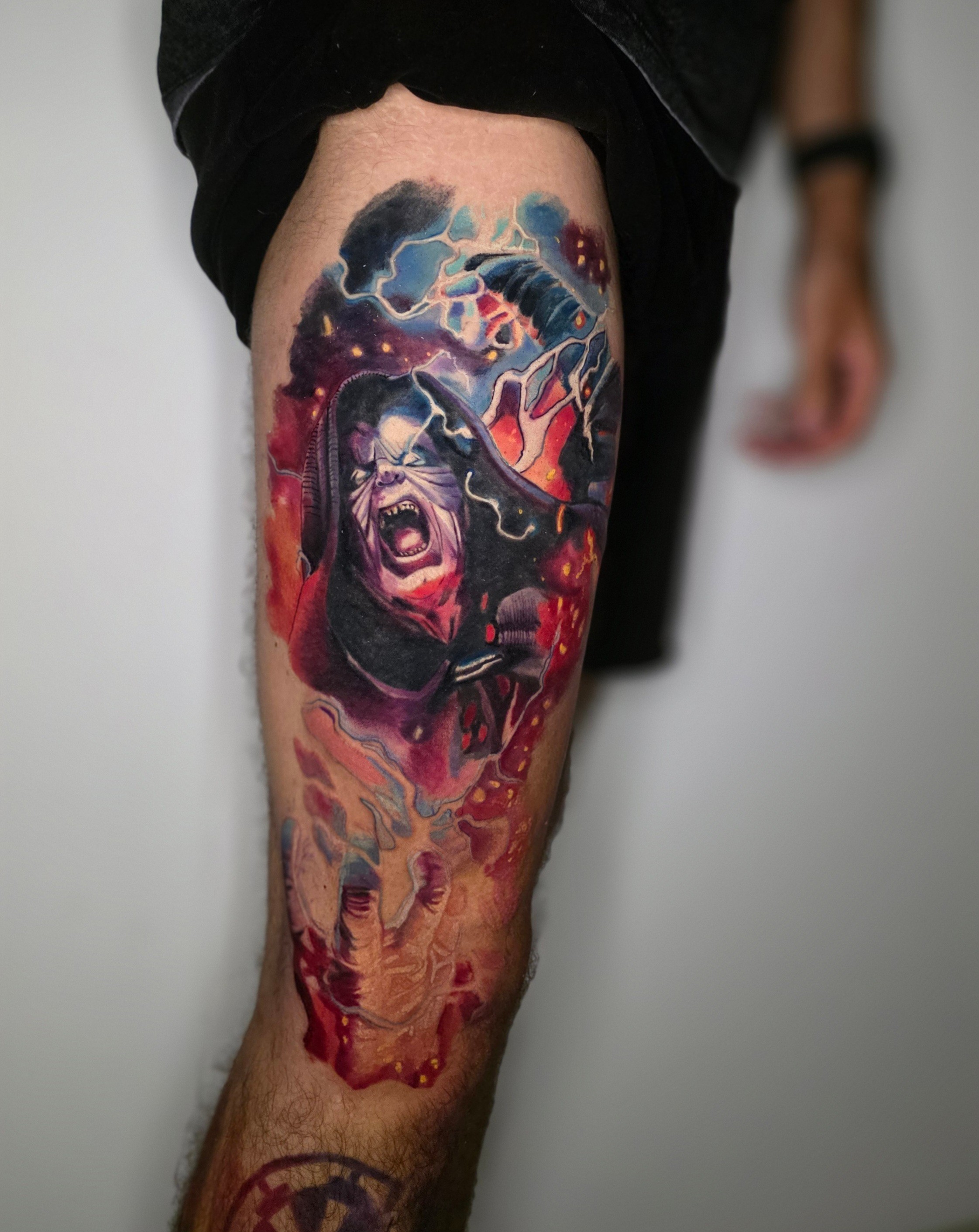 Colorful tattoo of a face with abstract elements on a person's thigh, with a background of dark clouds and lightning.