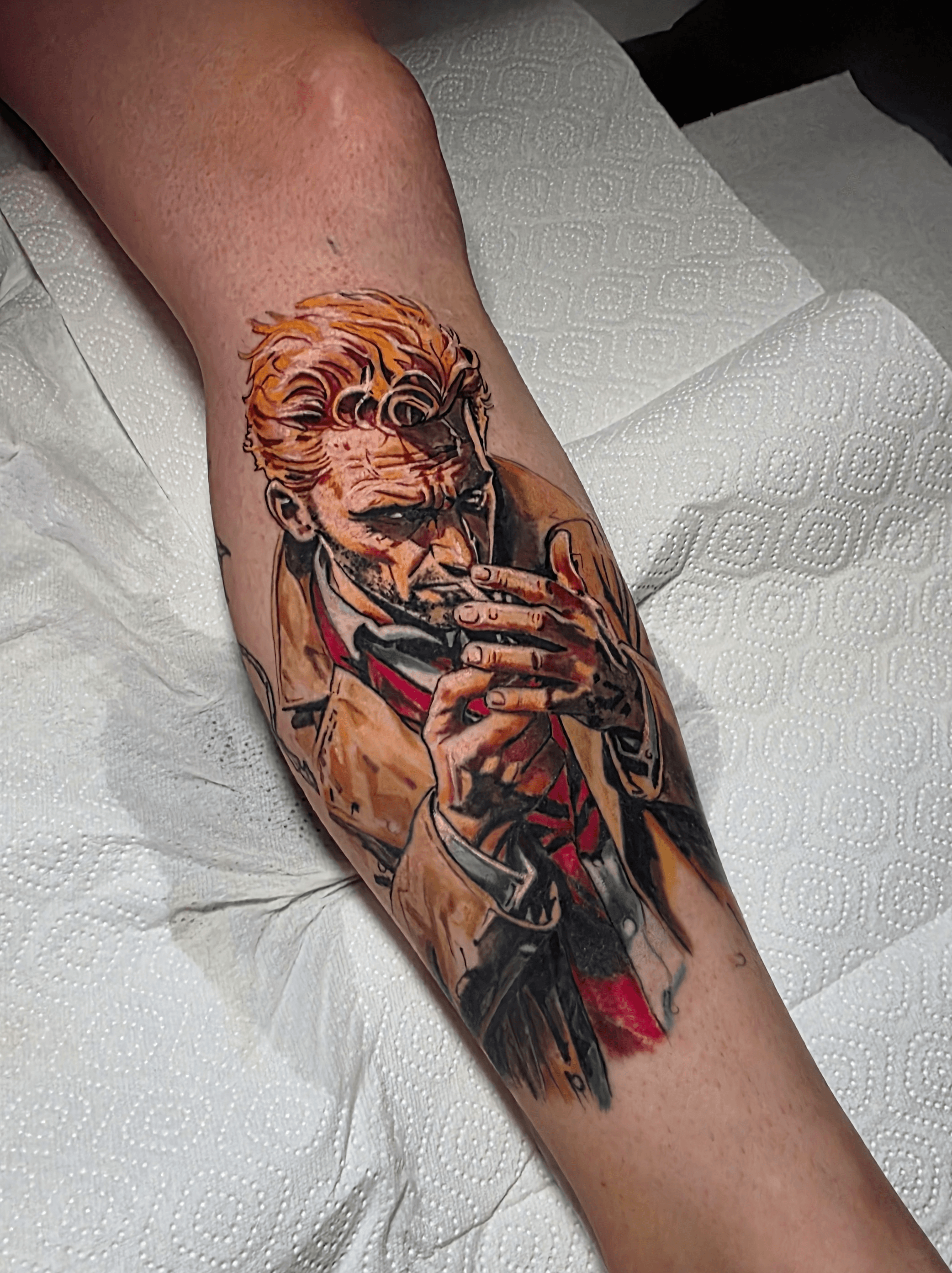 Tattoo of a man with colorful hair, holding a cigarette, wearing a suit and tie, on person's arm.