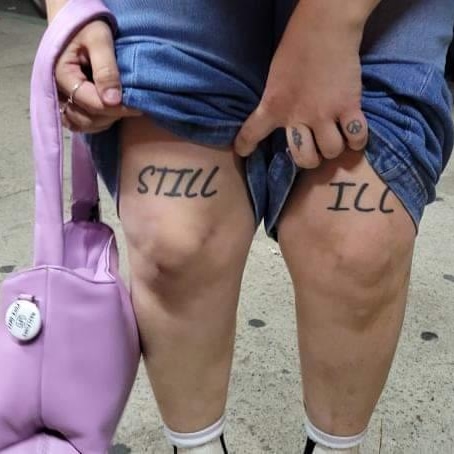 Person pulling up shorts revealing tattoos on thighs, holding a purple bag, on a concrete surface.