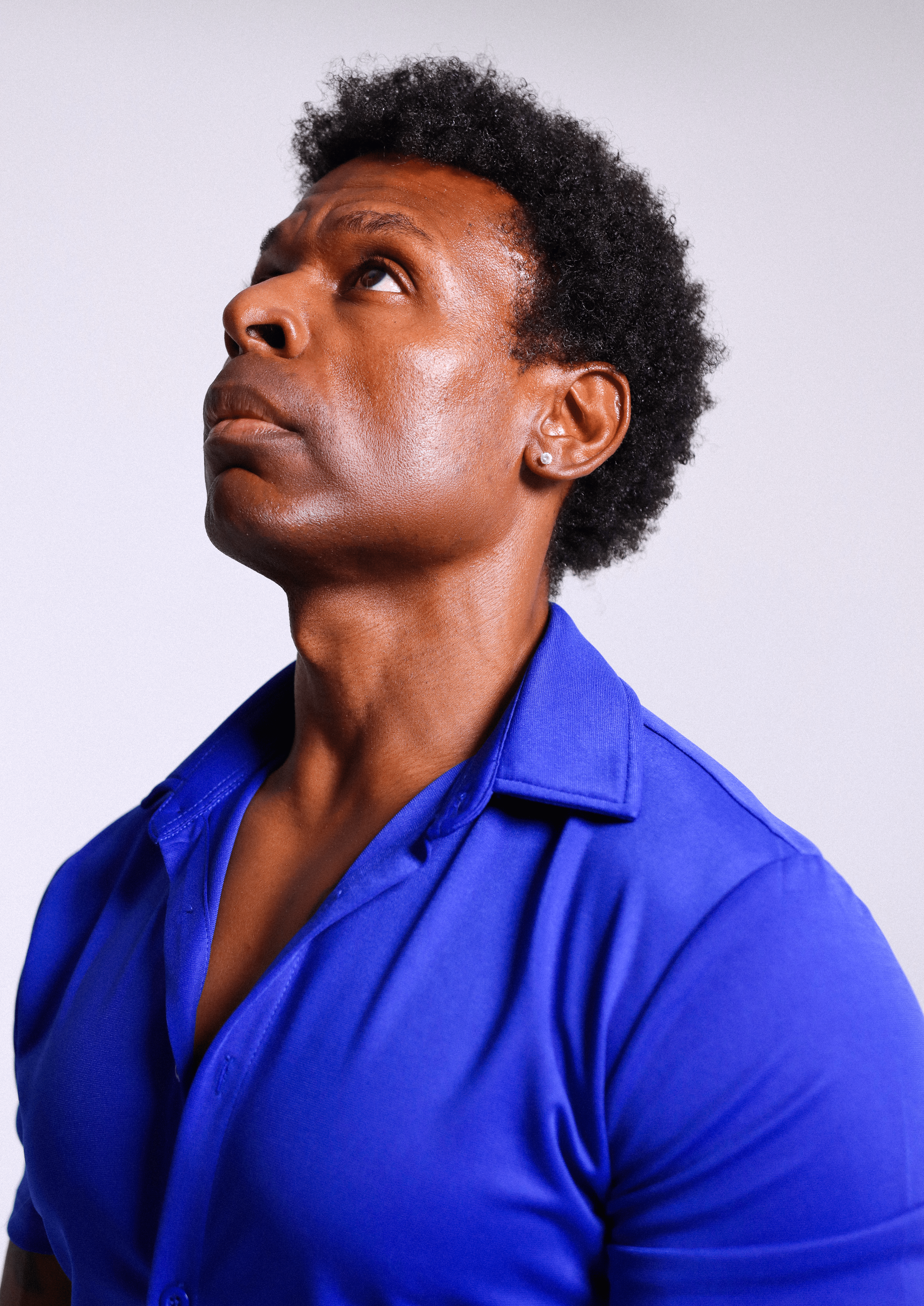 Person with short curly hair looking upward, wearing a blue shirt, against a plain light background.