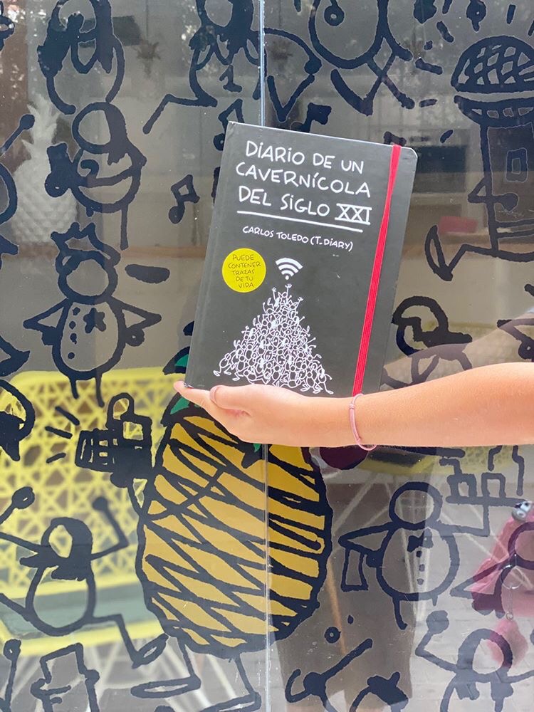 Person holding a book titled 'Diario de un cavernícola del siglo XXI' in front of a colorful, abstract background.