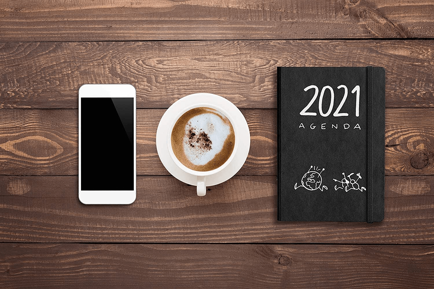 Smartphone, coffee cup, and 2021 agenda on wooden surface, top-down view.