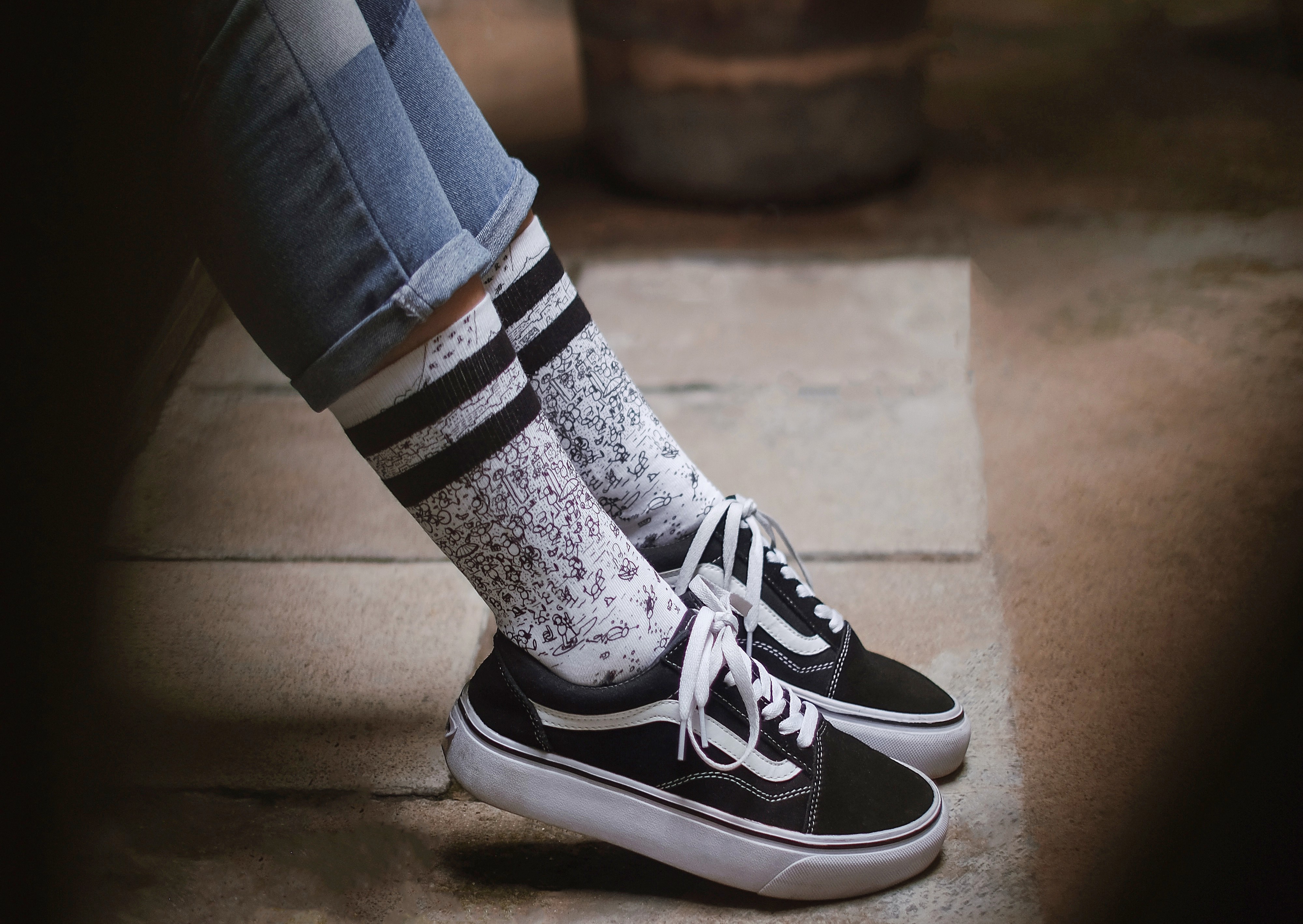 Person wearing sneakers and patterned socks, sitting with legs crossed on a wooden floor.