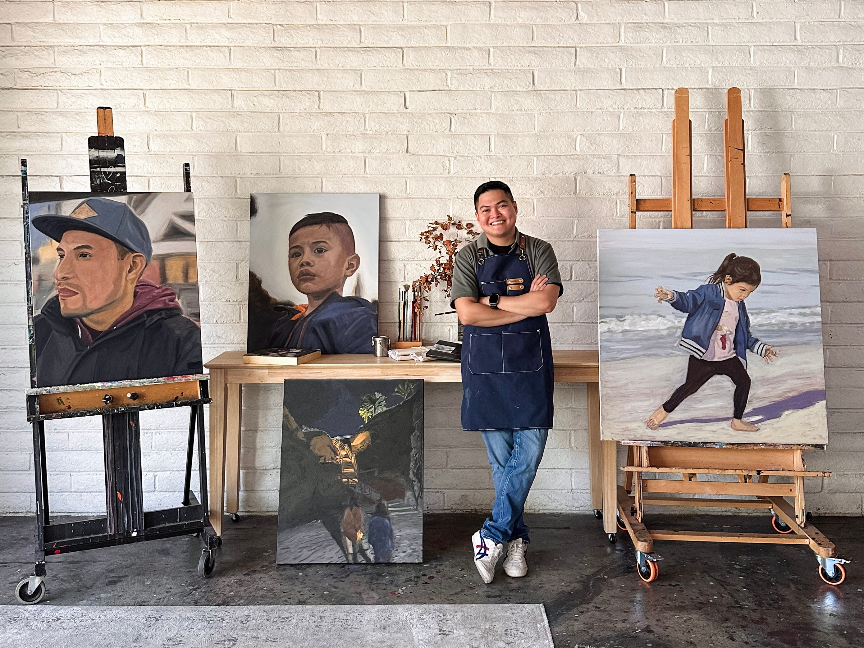 Four paintings of children and a man in an art studio with a white brick wall background.