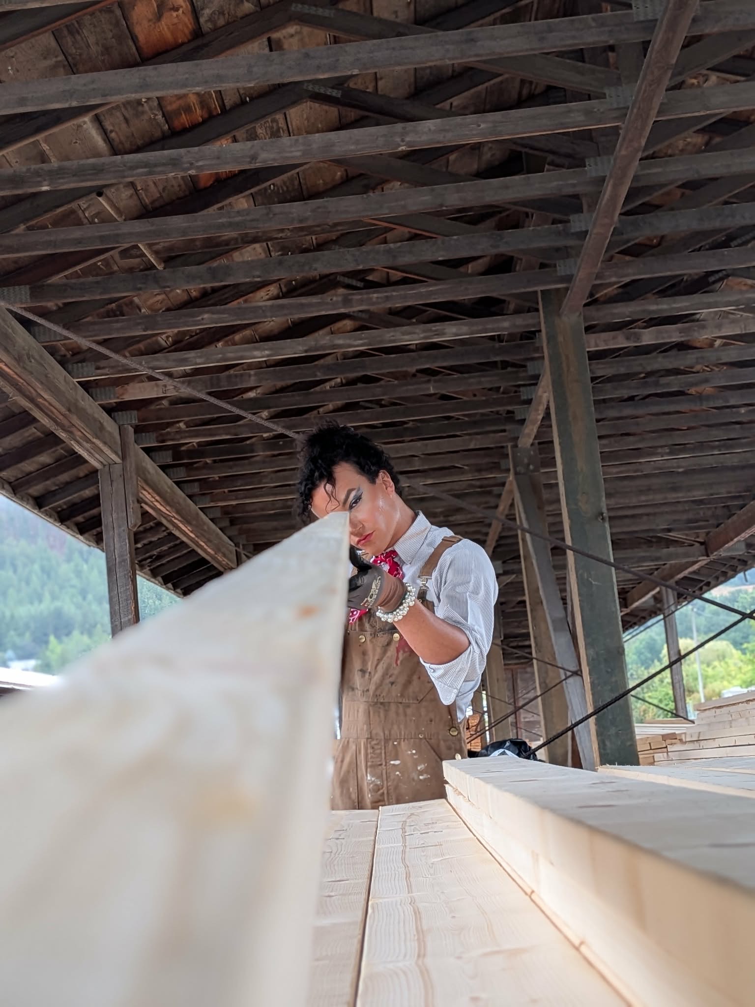 Person working with wood in a rustic, open-air workshop with a wooden roof and beams.
