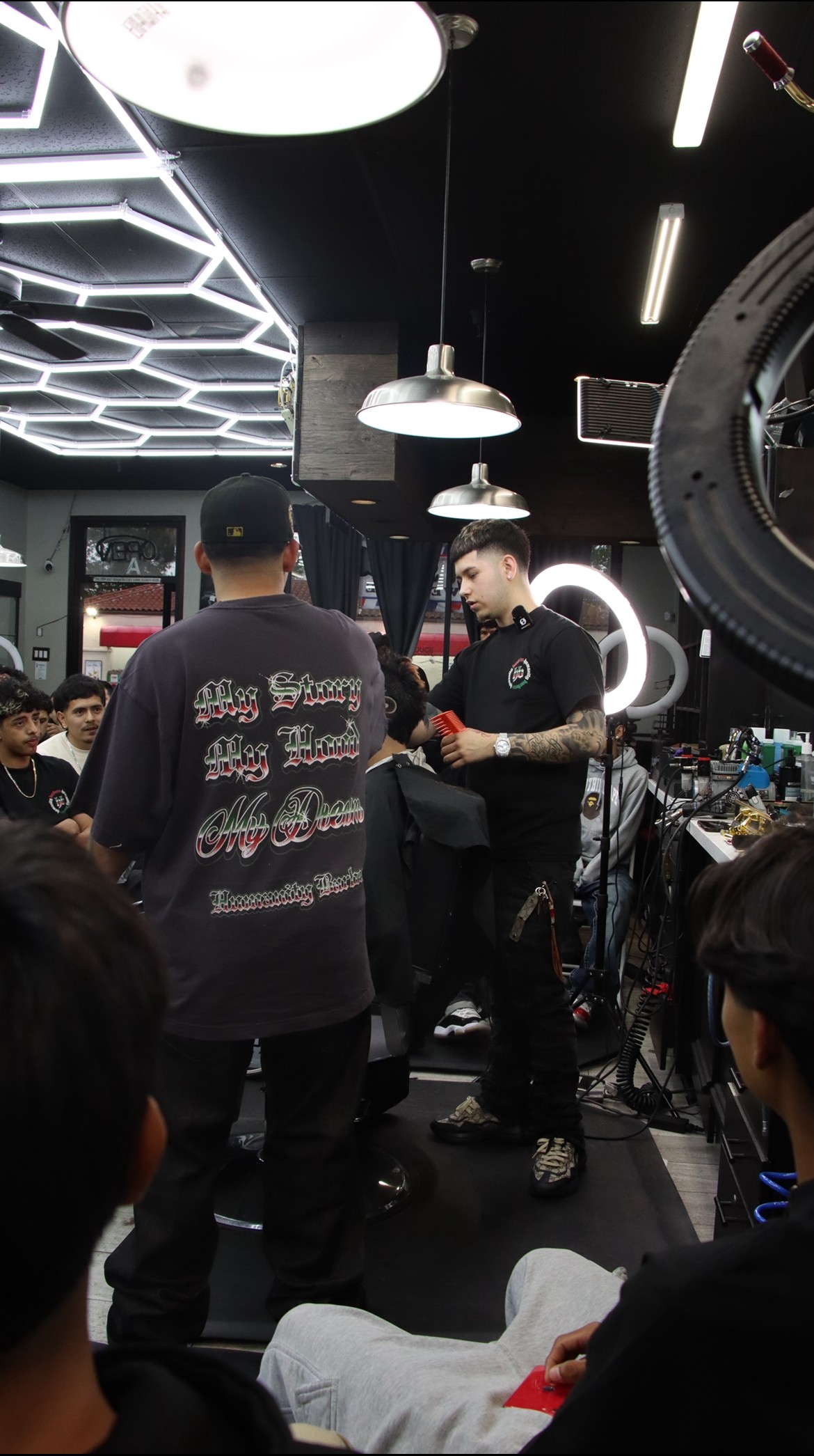 People gathered in a modern indoor space with black walls and geometric ceiling lights, some standing and others seated, engaging in conversation.