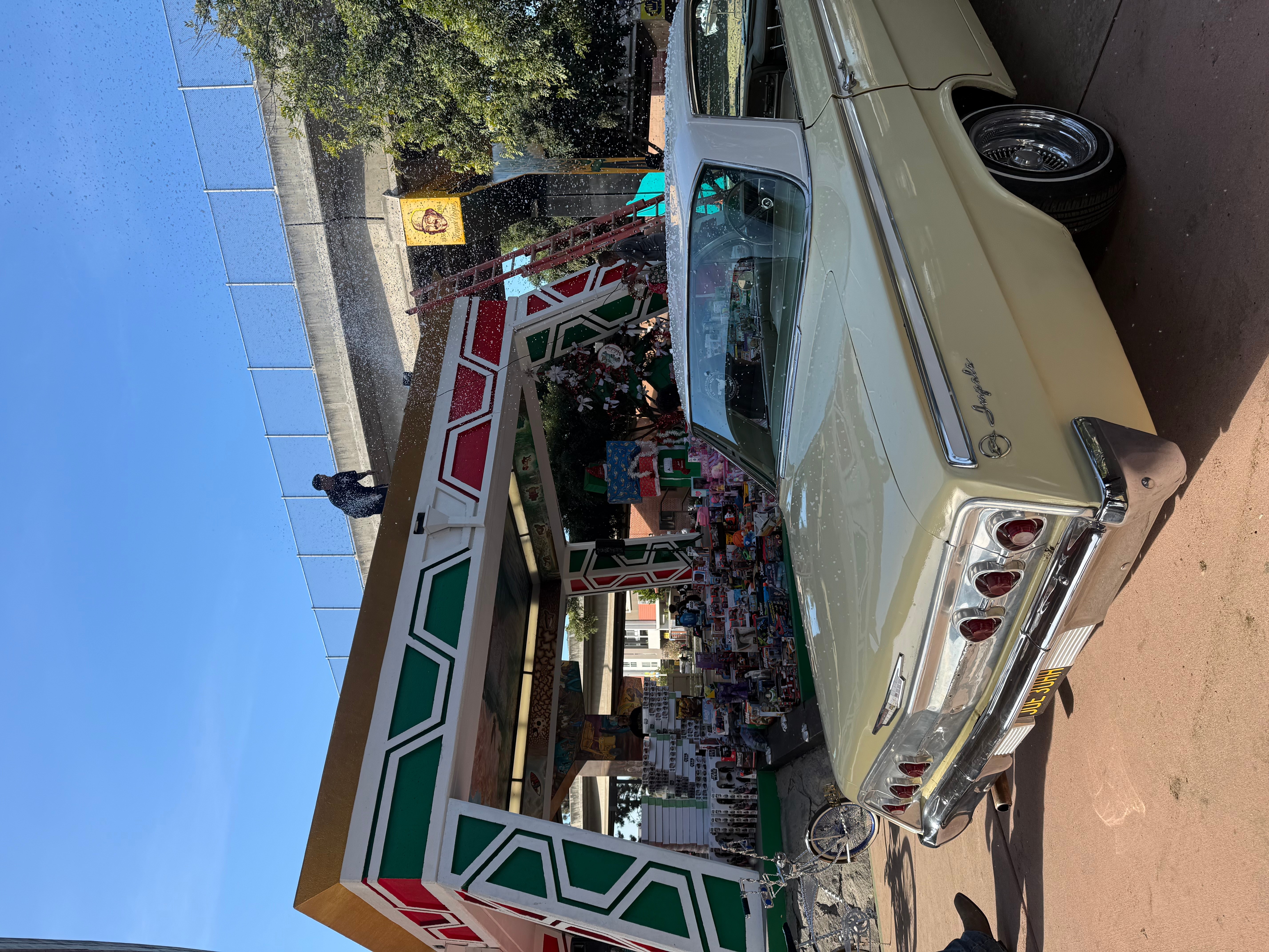 A vintage car parked in front of a decorated building with a person standing nearby, under a clear blue sky.