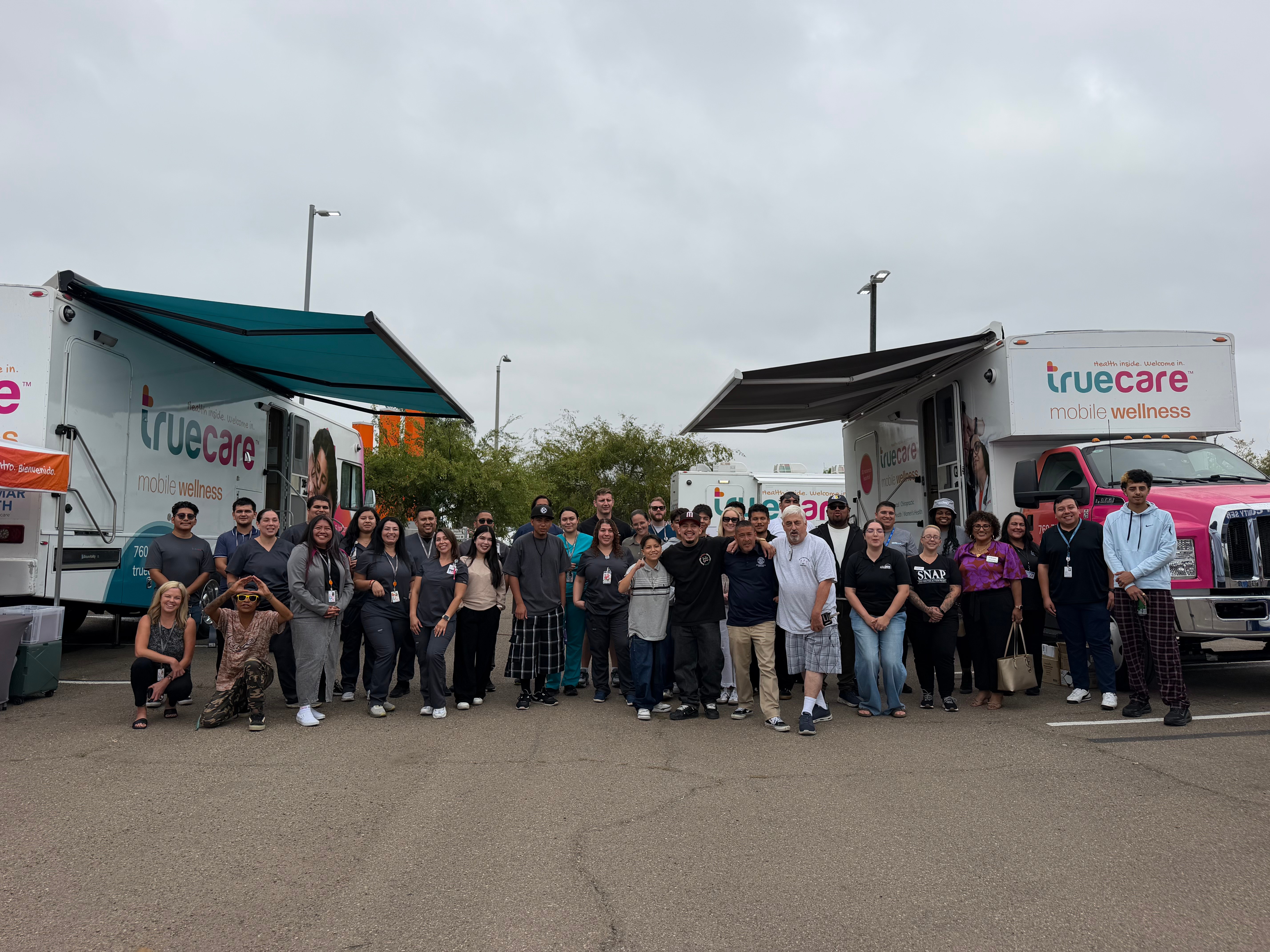 Group of people standing in front of two mobile healthcare trucks outdoors on a cloudy day.