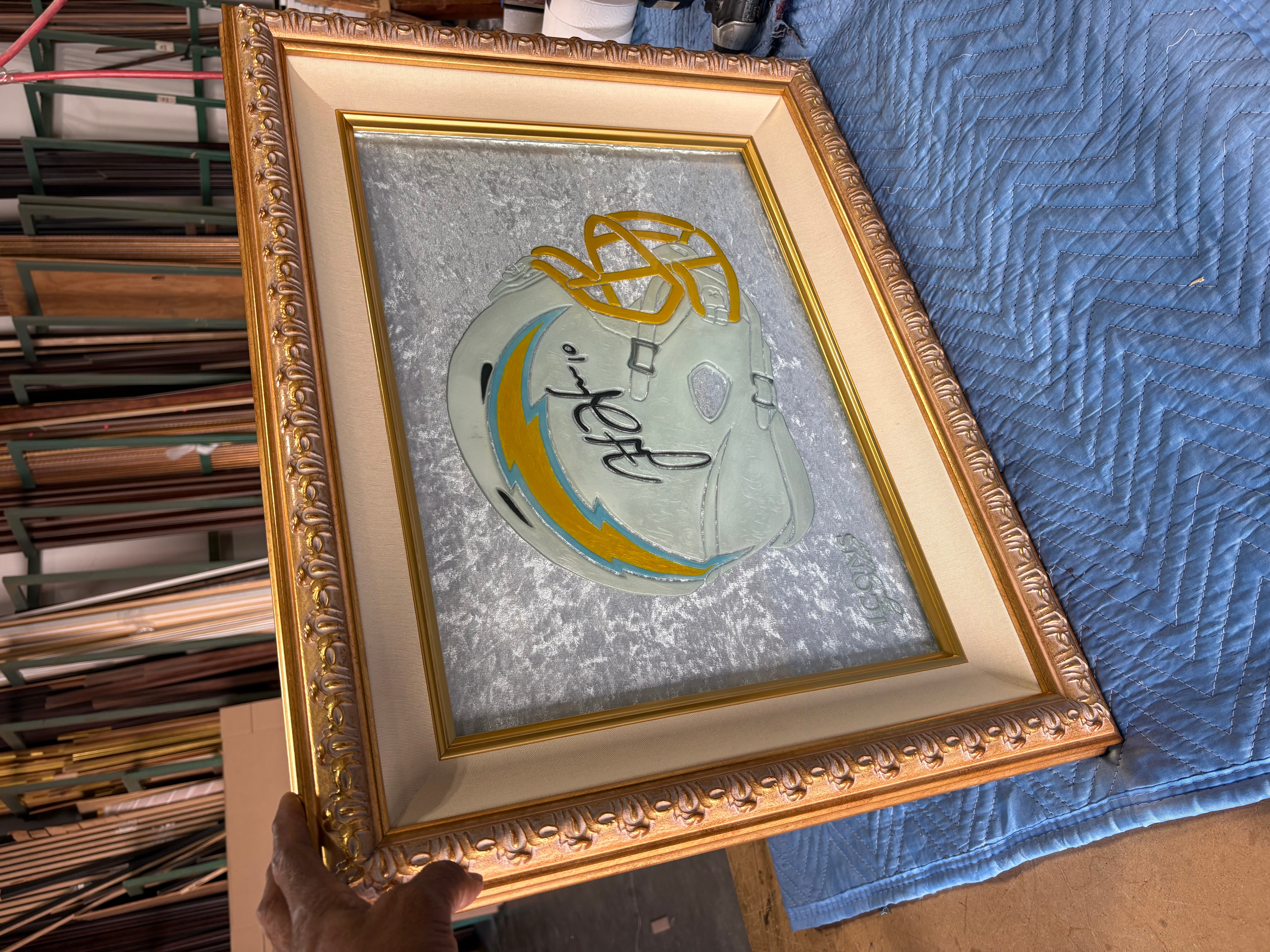 Decorative framed mirror with gold ornate border, reflecting a circular design with text, placed on a blue fabric surface.