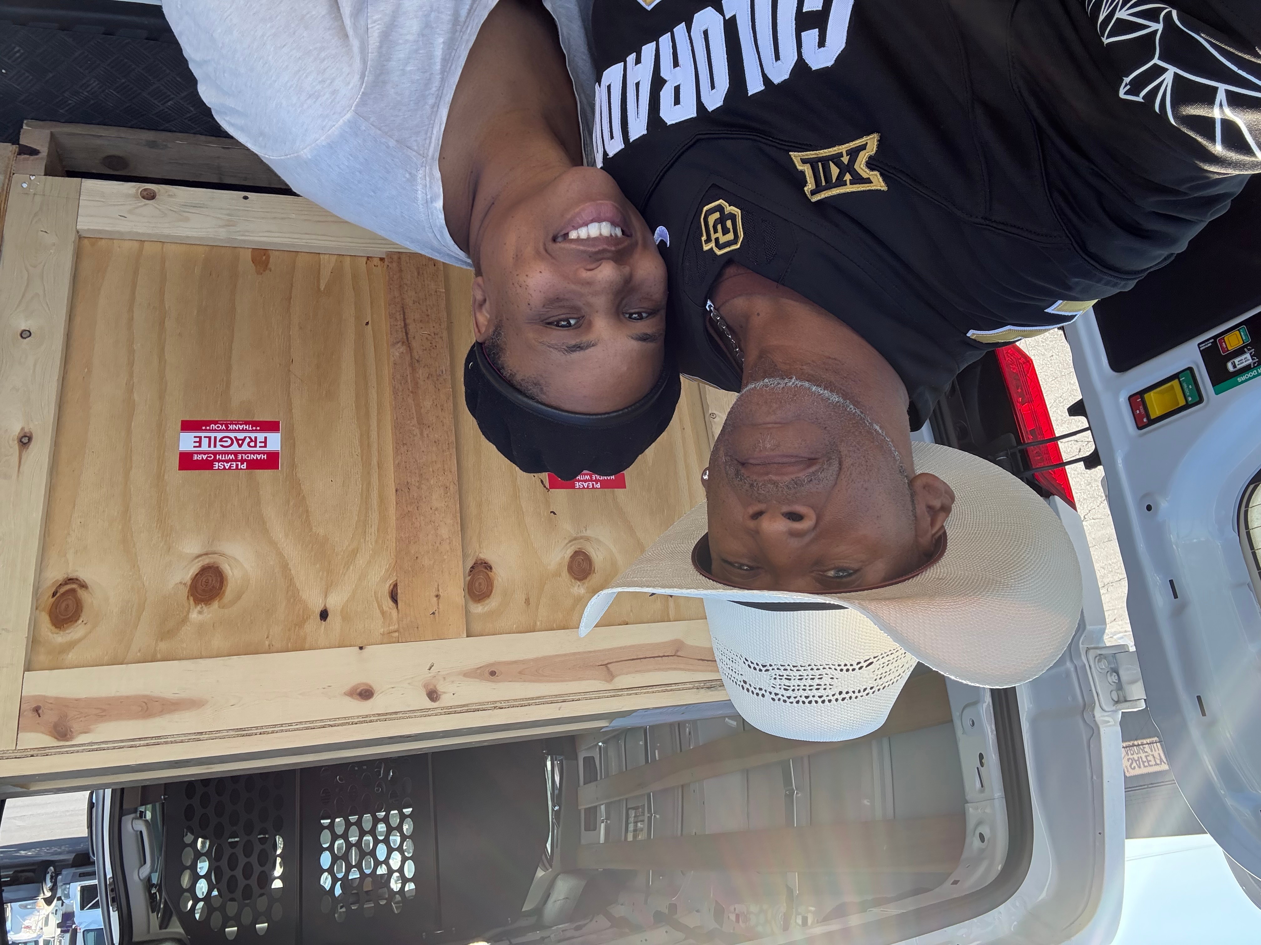 Two people lying on the ground, one wearing a white cap and the other in a black shirt, smiling at the camera.