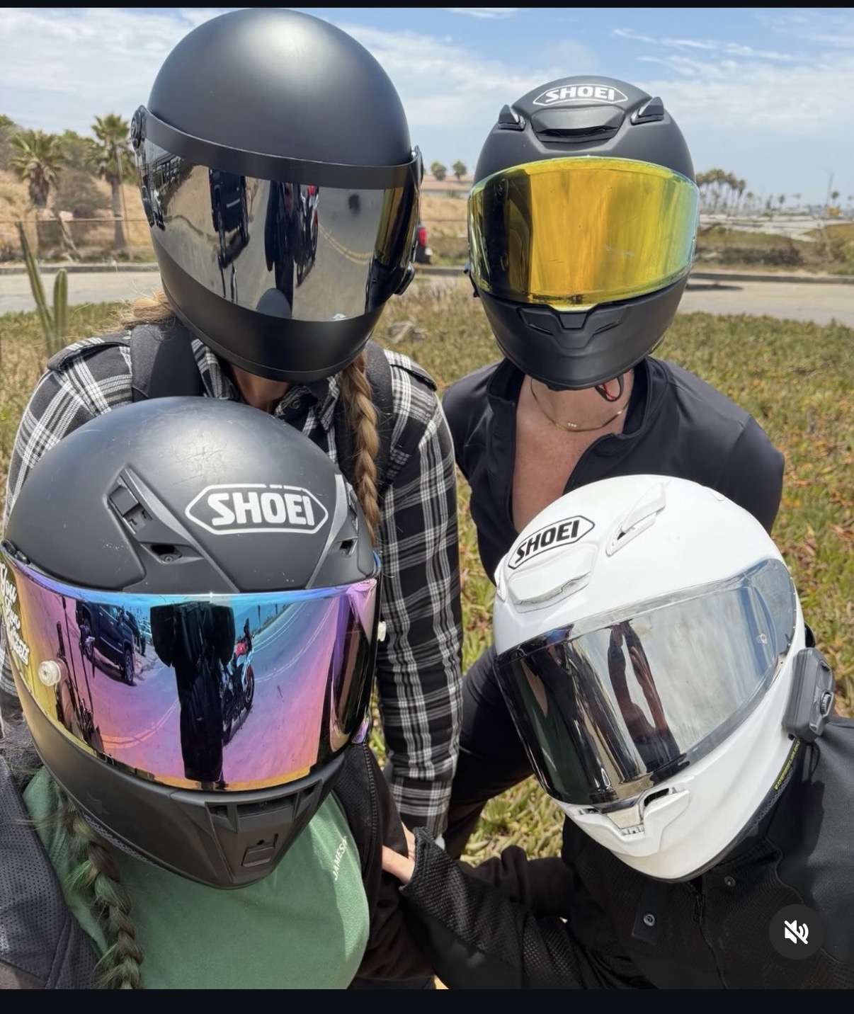 Four people wearing motorcycle helmets outdoors, with a background of trees and a clear sky.