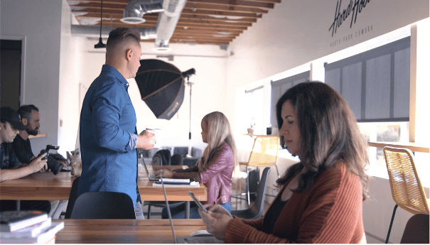 People in a modern office or studio, some working on laptops, one person standing, another sitting and using a phone.