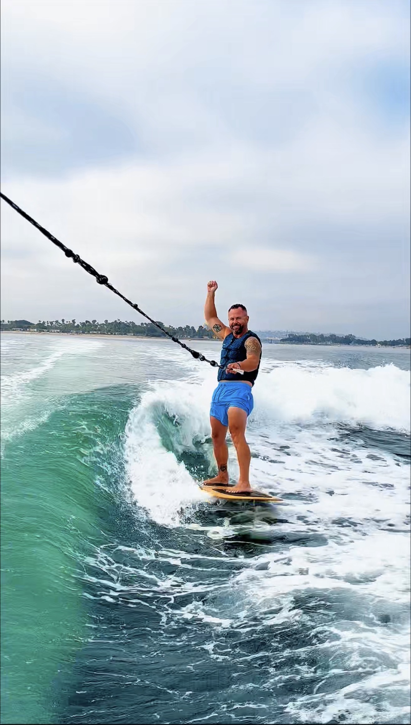 Person wakeboarding on water, holding rope, wearing life vest and shorts, with cloudy sky background.
