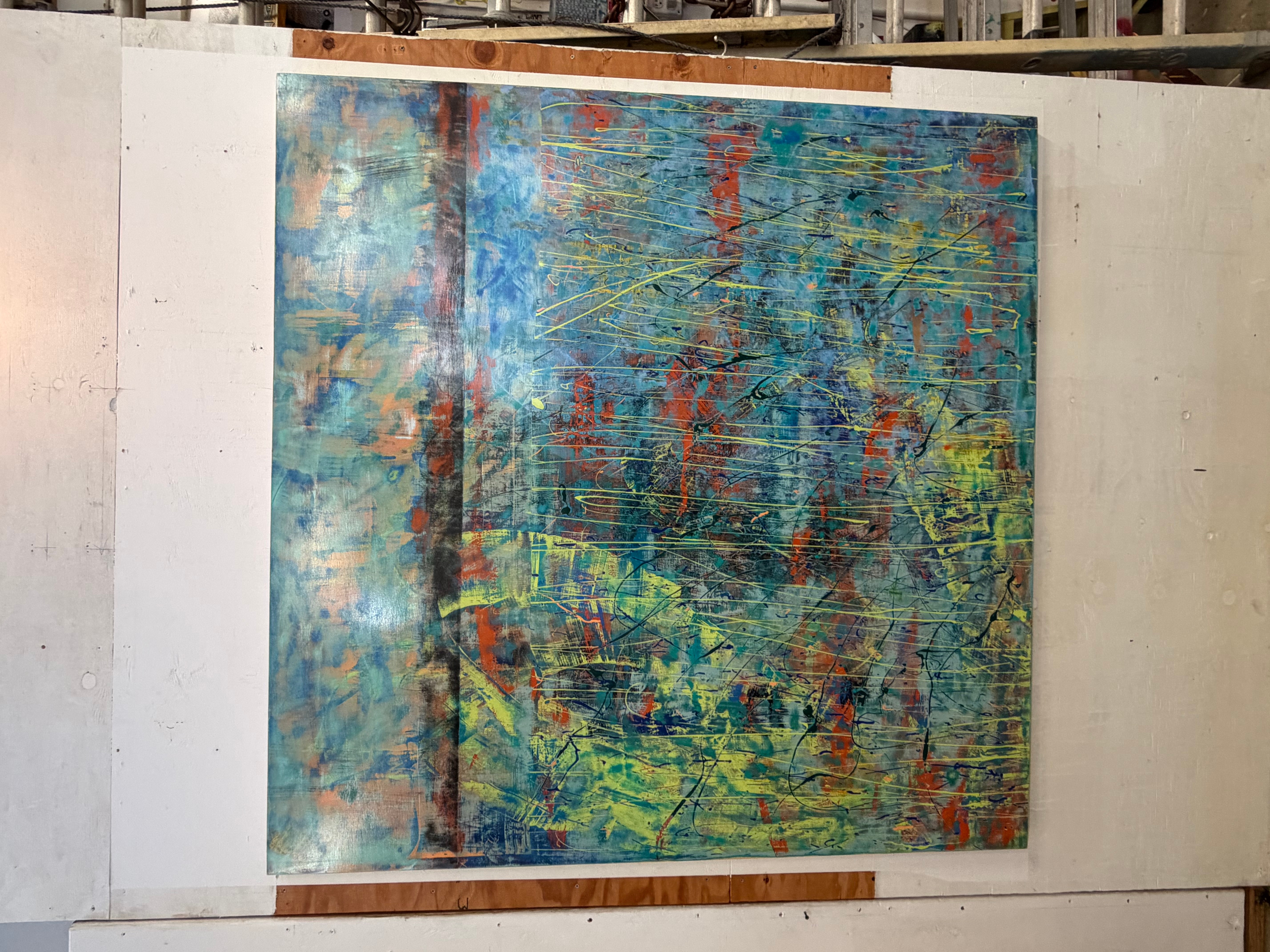 Abstract painting with blue, green, red, and yellow colors on a canvas, displayed on a white wall.