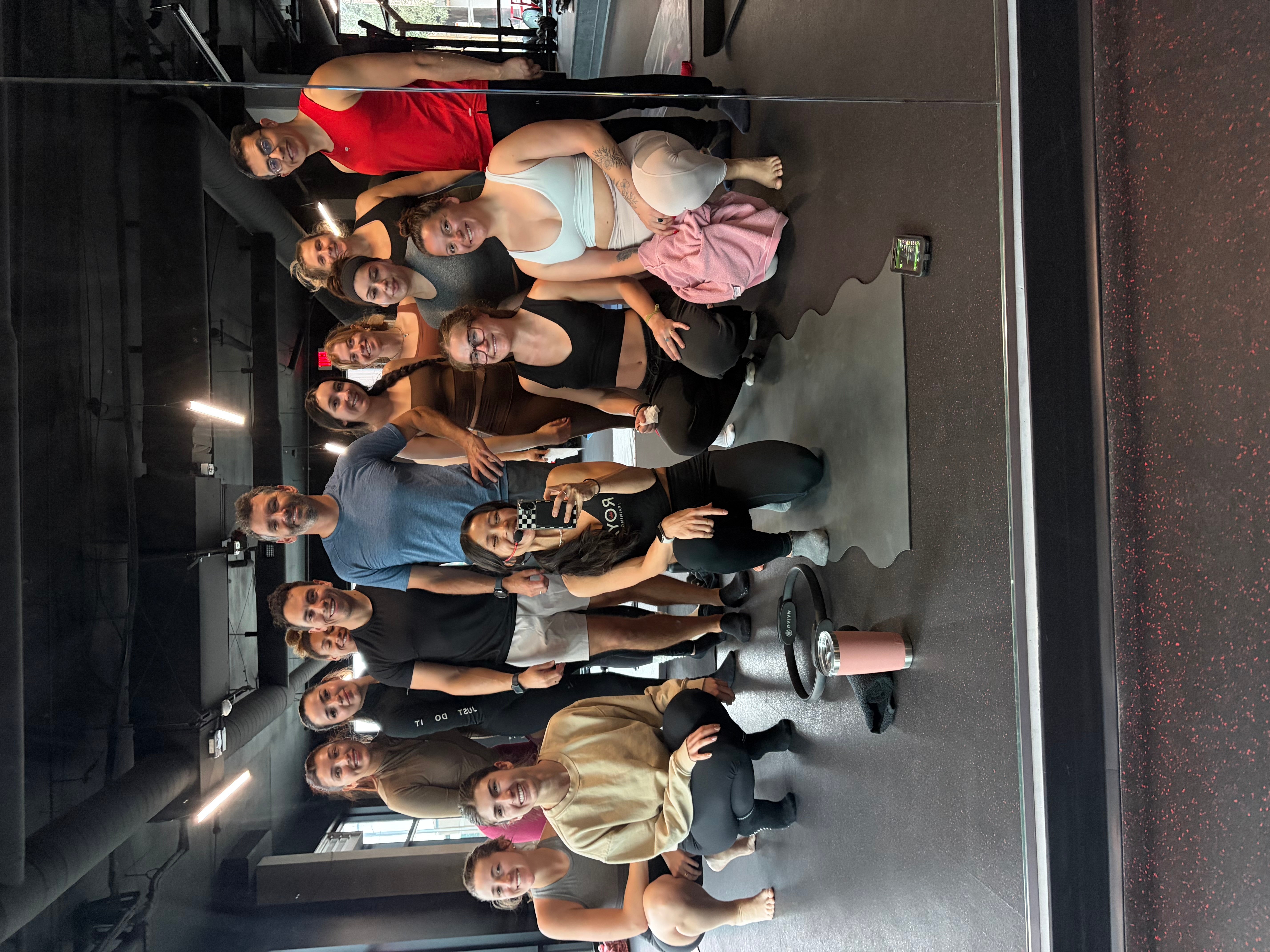 Group of people posing for a photo in an indoor setting, some sitting and some standing, with a dark background.