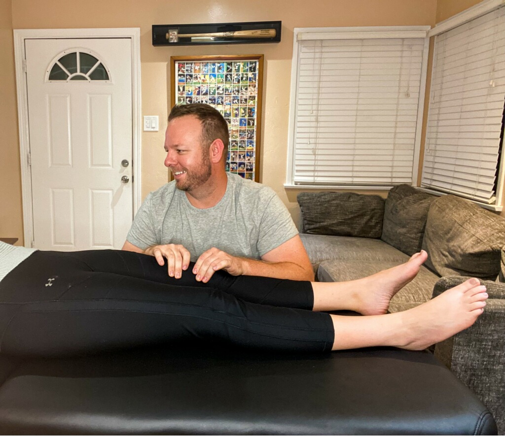 Man smiling and holding a person's legs on a black surface in a living room with a couch and windows