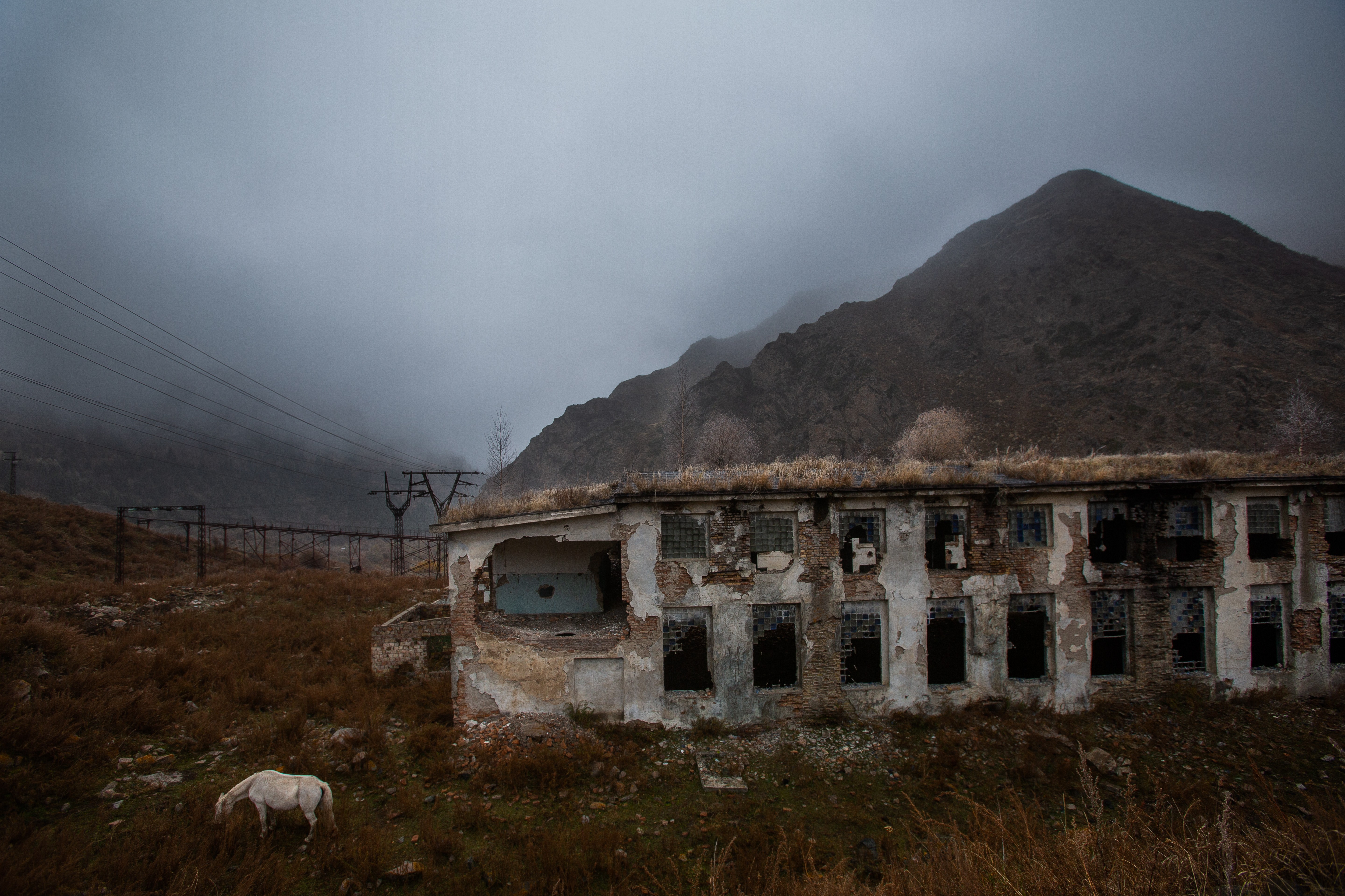 Ruined building in a grassy field with a mountain and cloudy sky in the background.