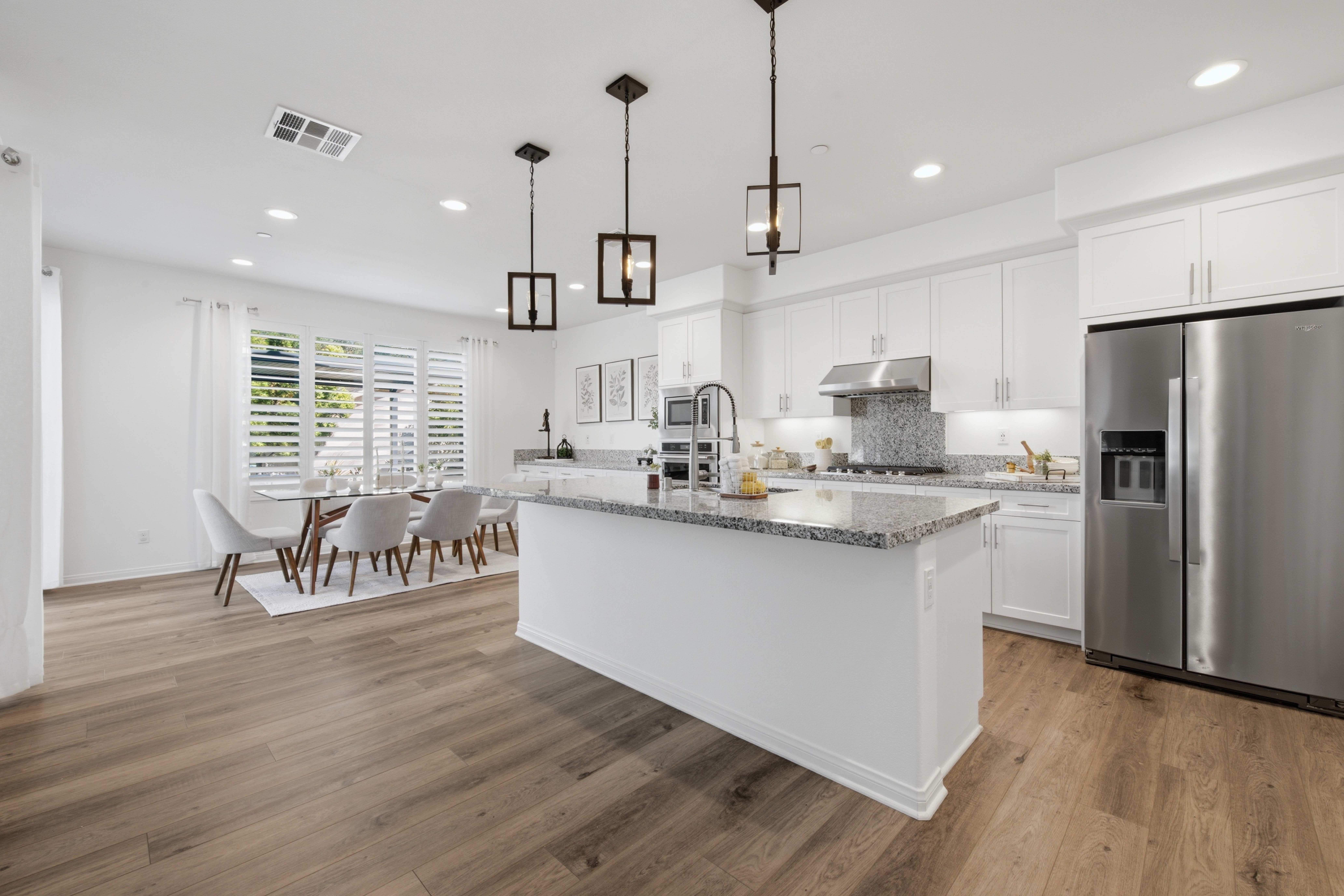 Modern kitchen with white cabinets, stainless steel appliances, island, and dining area with table and chairs, hardwood floors, and large windows.