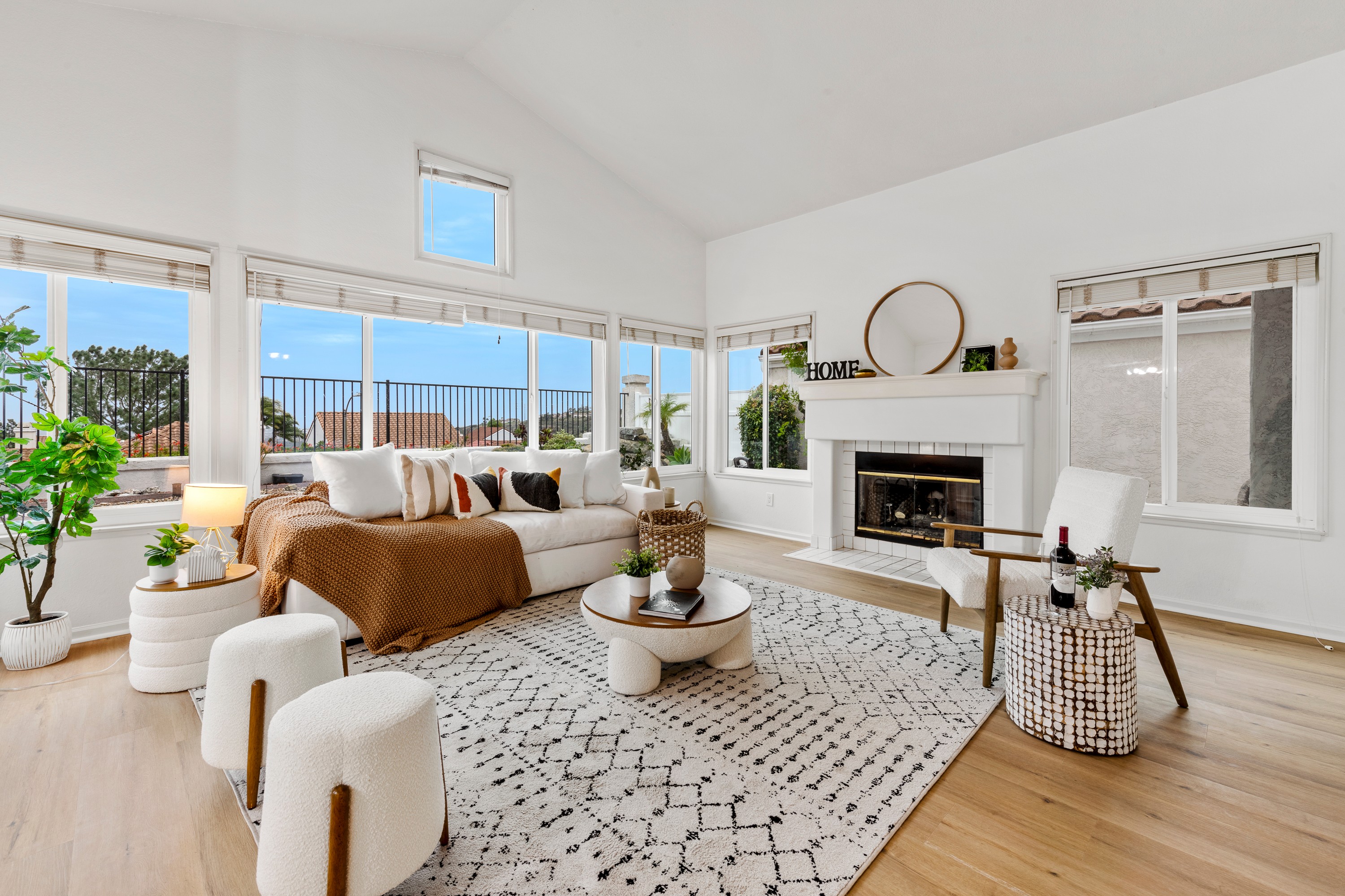 Bright living room with large windows, white walls, a fireplace, and modern furniture including a sofa, ottomans, and a rug.