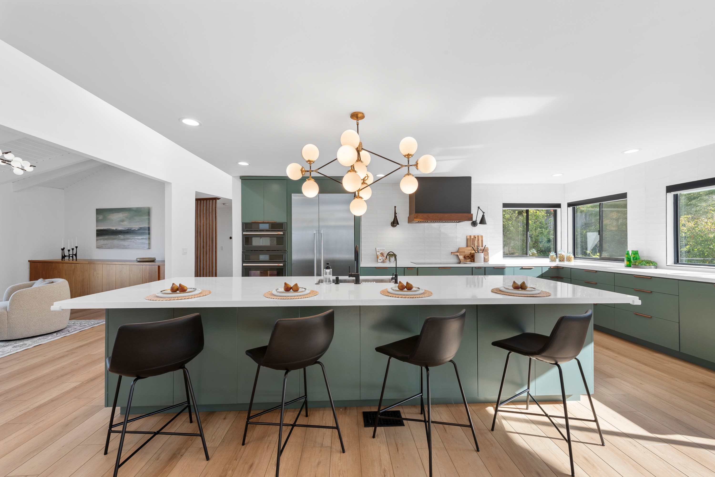 Modern kitchen with a large island, black chairs, and a chandelier, bright with natural light from windows.