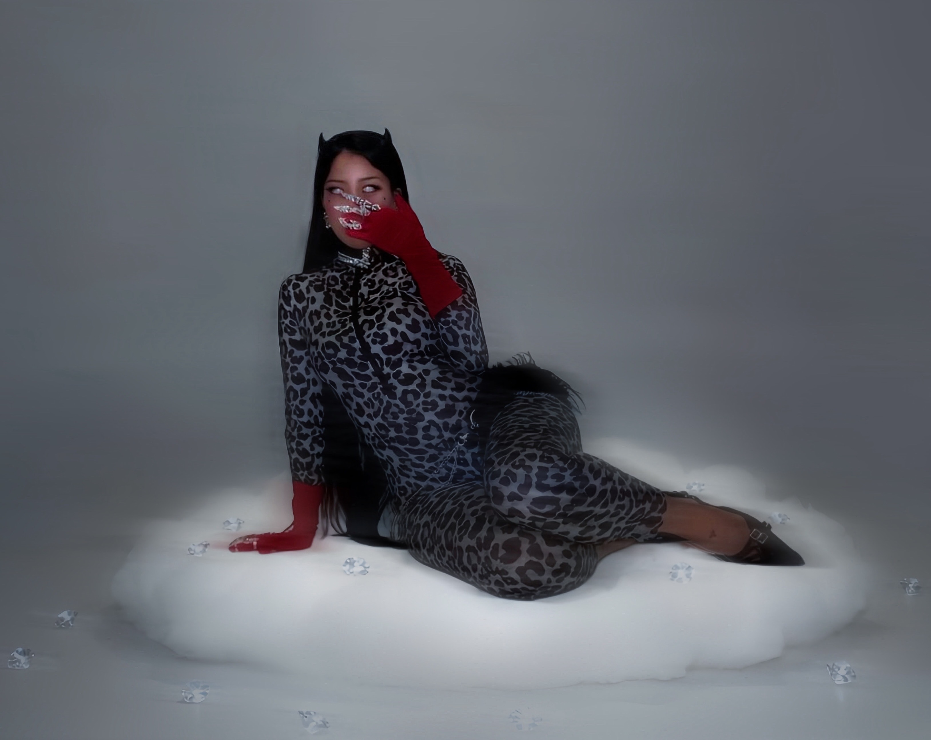Person lying on a white surface, wearing a leopard print outfit and red gloves, with a gray background.