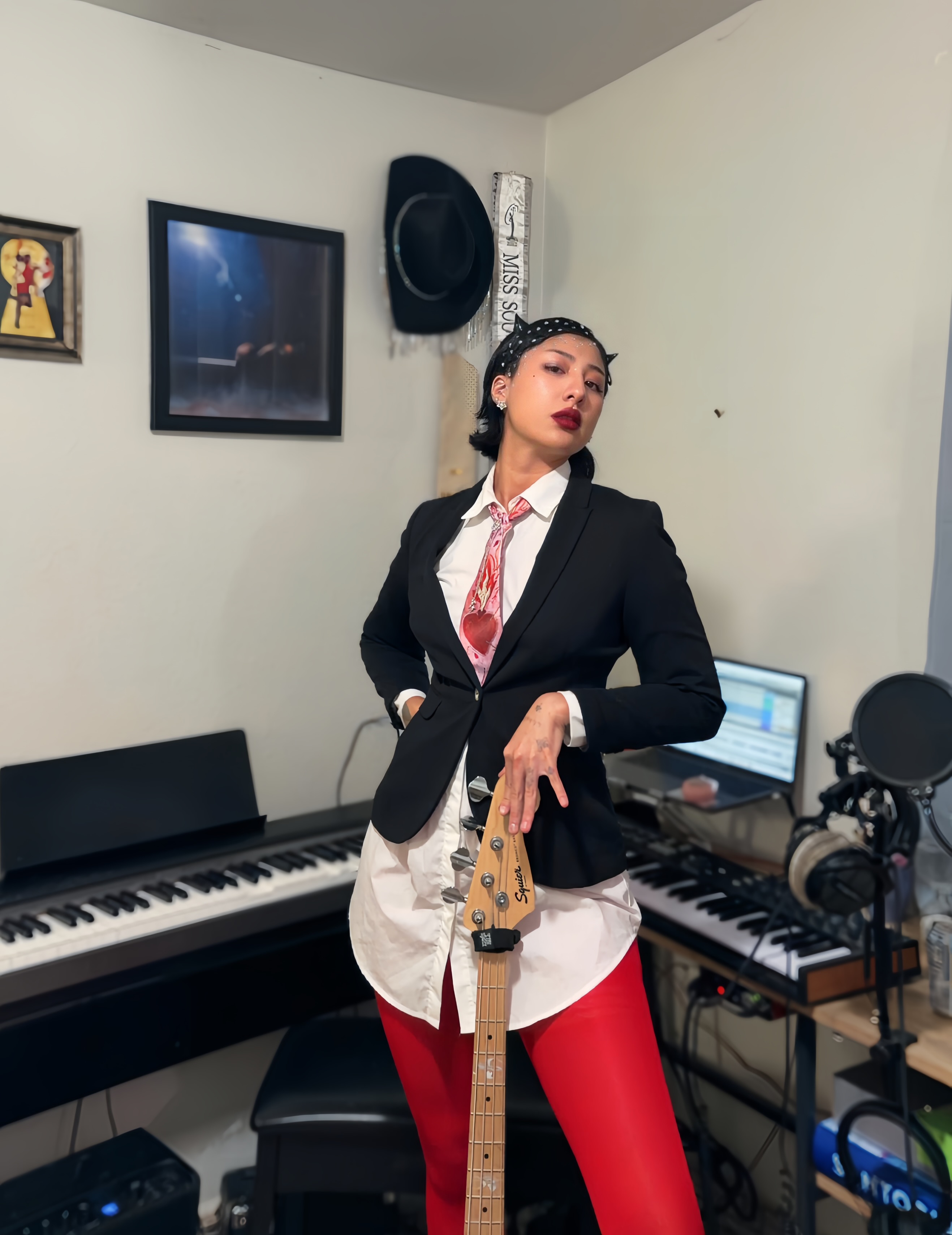 Woman in a black blazer and red pants standing in a music studio with keyboard and computer.